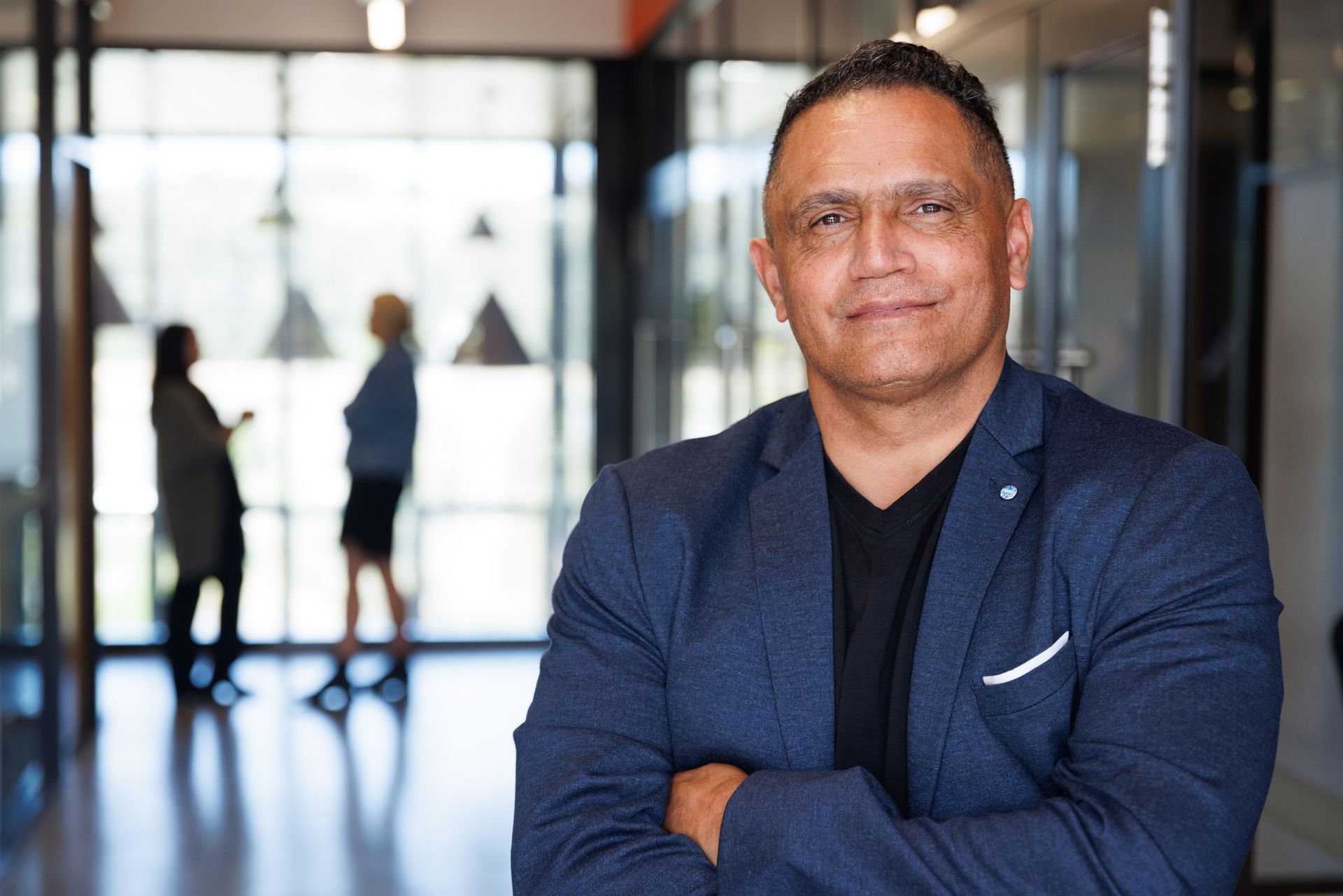 A man in a suit is standing with his arms crossed in front of a window.