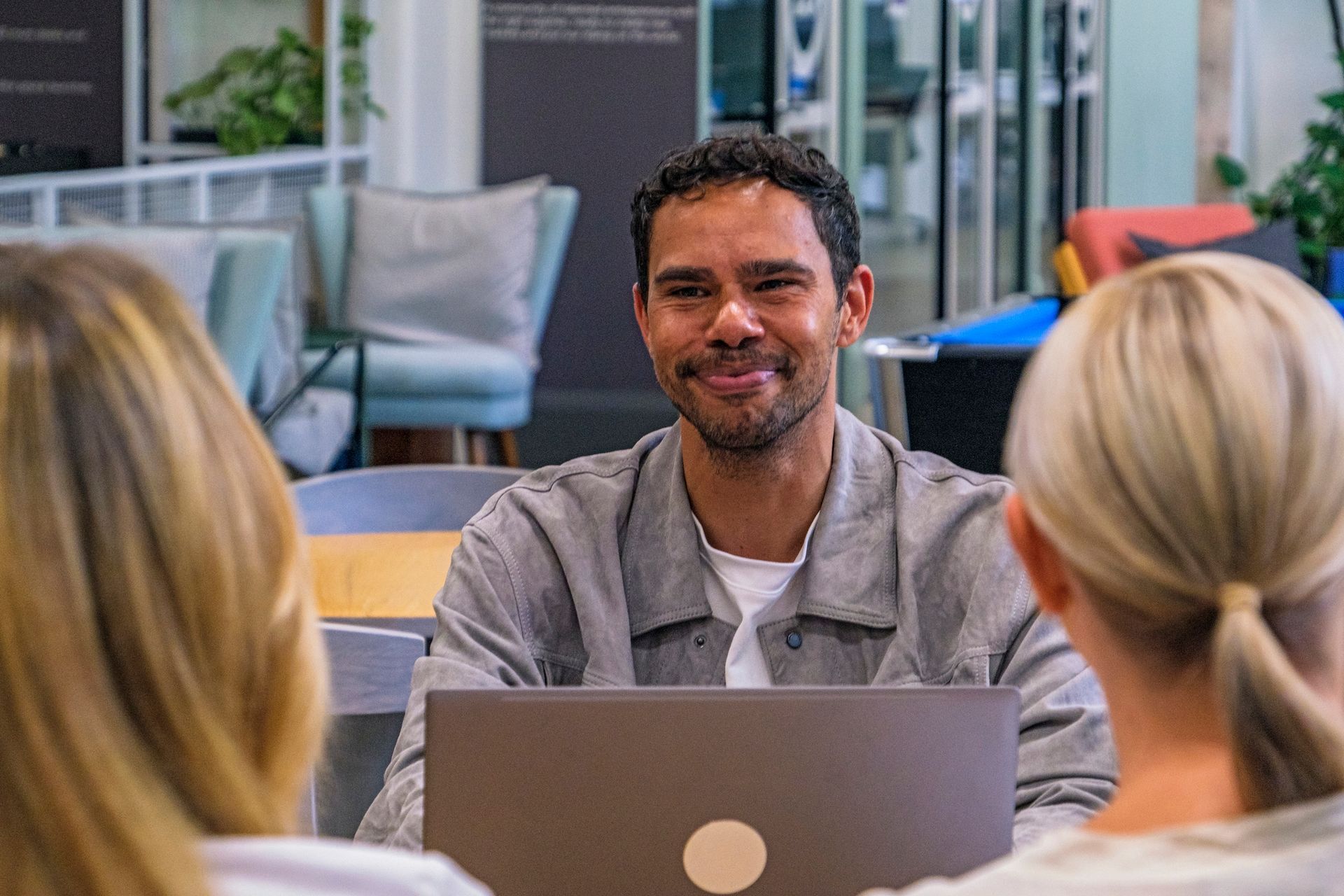 A man is sitting at a table with two women while using a laptop computer.