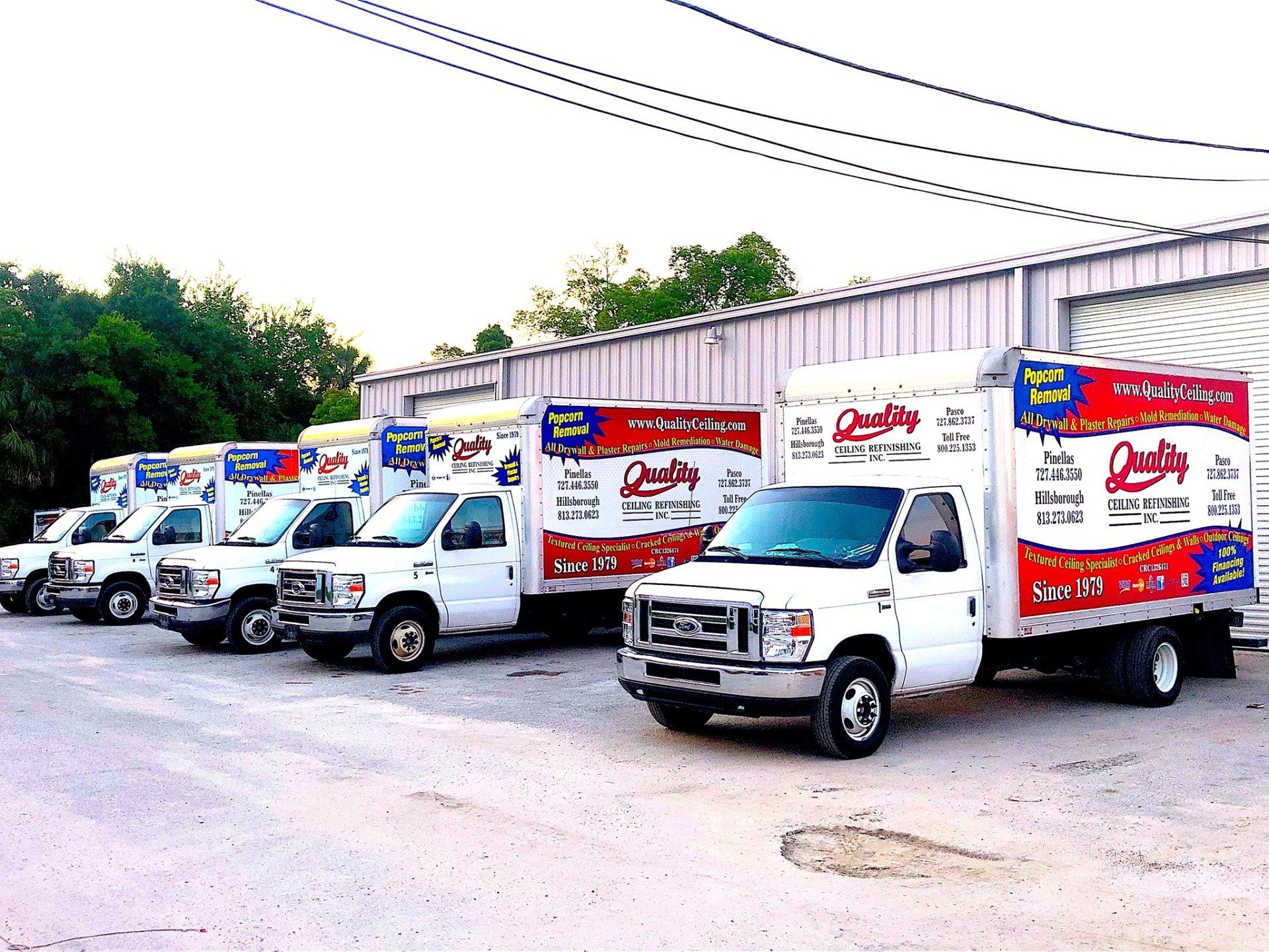 Line of white box trucks with company logo parked in front of a building.