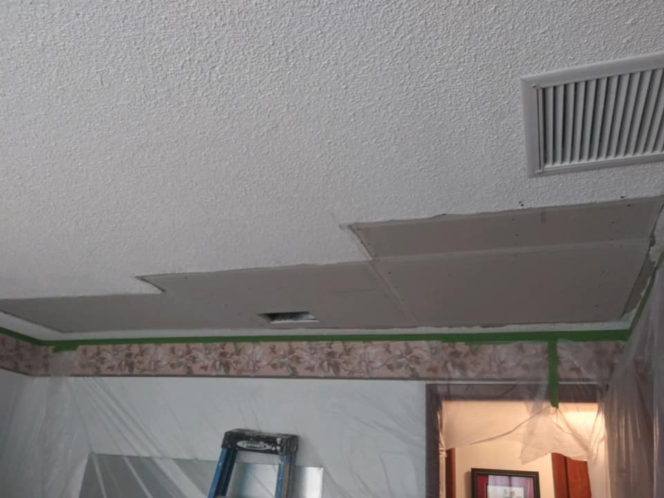 Ceiling with damaged drywall being repaired; tape on wallpaper, air vent, and ladder visible.