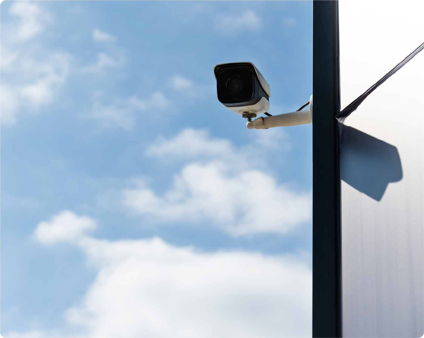 A security camera is hanging from a pole with a blue sky in the background