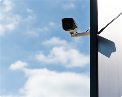 A security camera is hanging from a pole with a blue sky in the background.