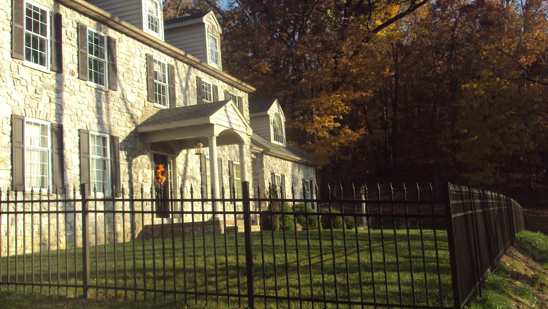 Stone house with black fence, green lawn, autumn trees.