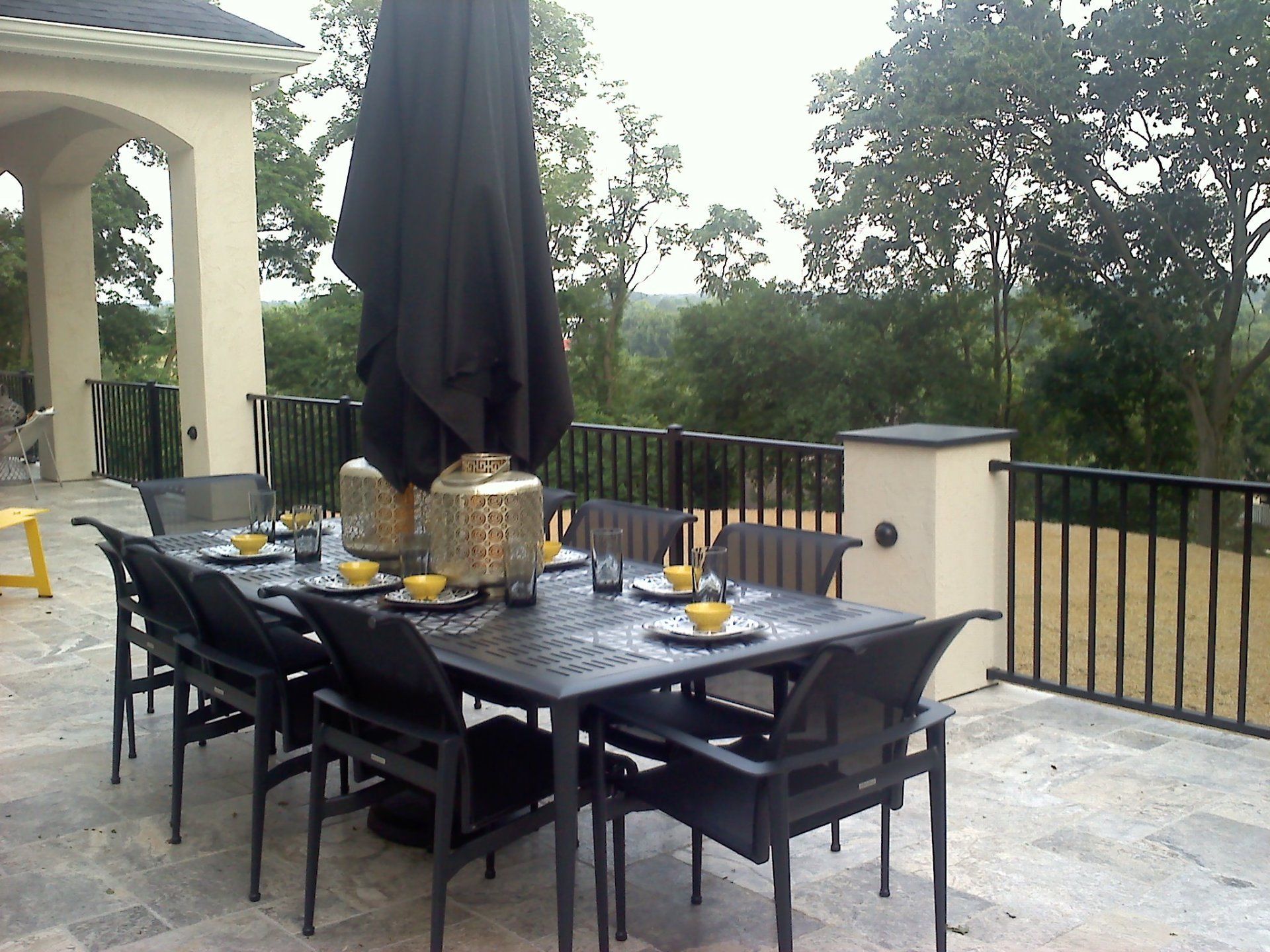Patio dining set with black umbrella, on a stone patio overlooking a green landscape.