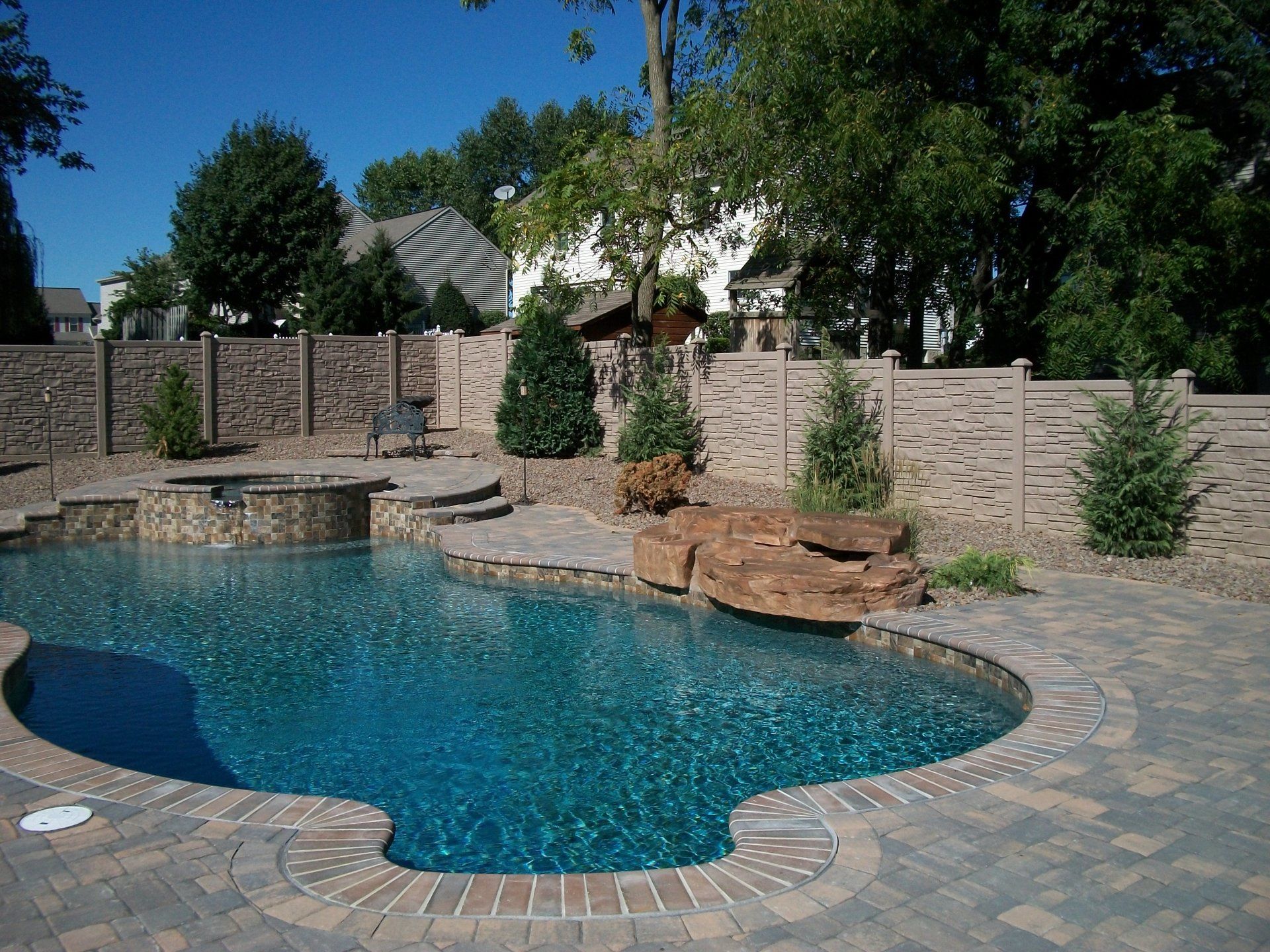 Swimming pool with a stone patio, landscaping, and a brick fence.