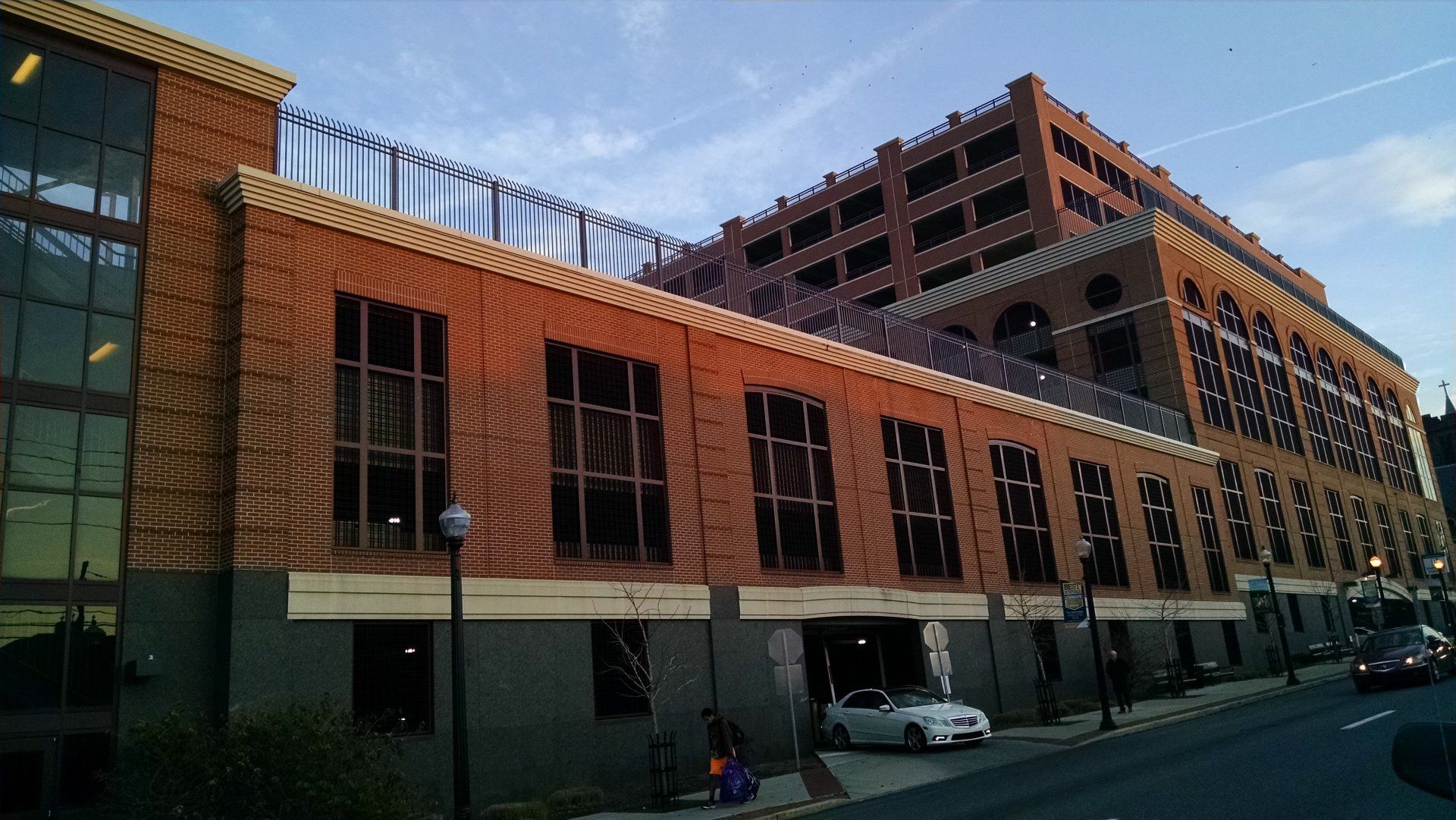 Brick building with large windows and a parking garage in the background. A car is parked on the street.