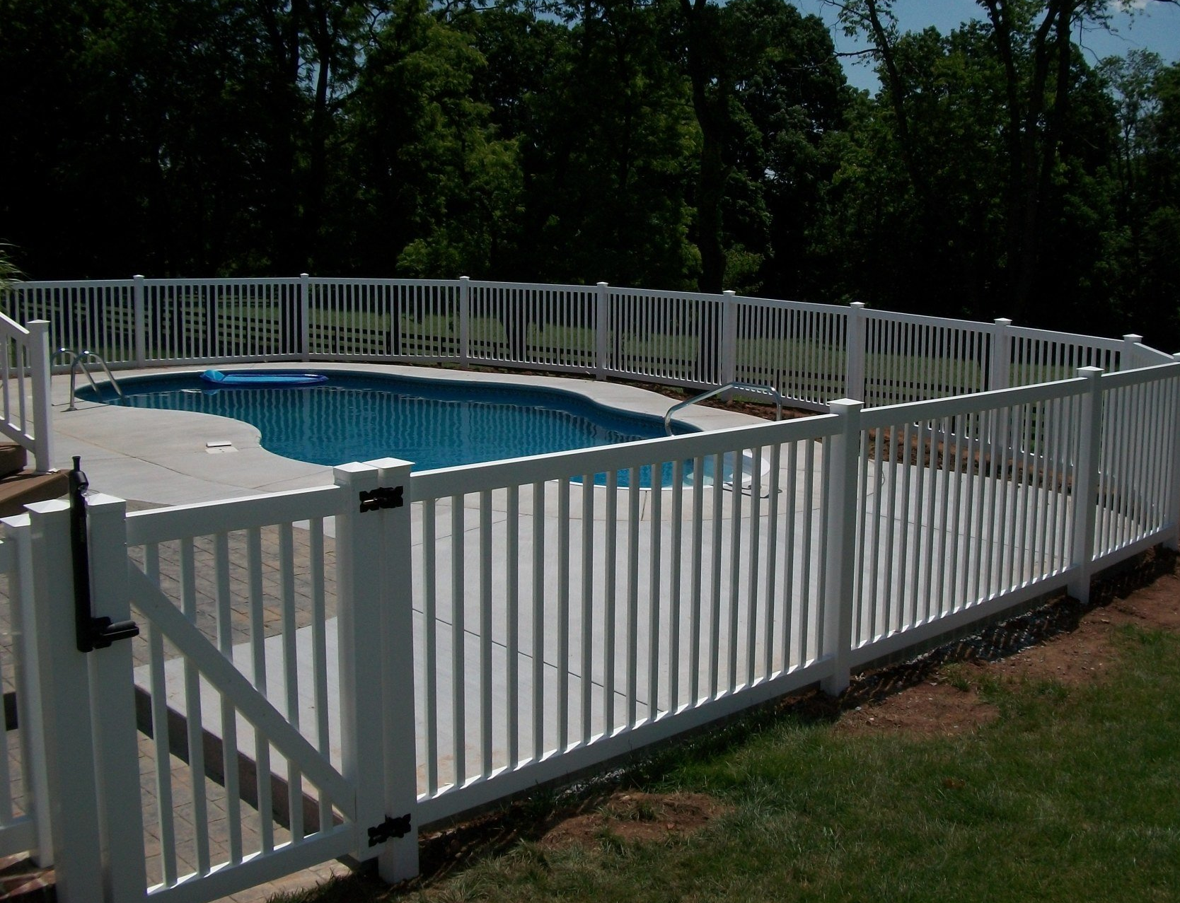 White fence by Millcreek Fence & Decks that surrounds a blue, kidney-shaped swimming pool in a grassy yard, under a sunny sky.