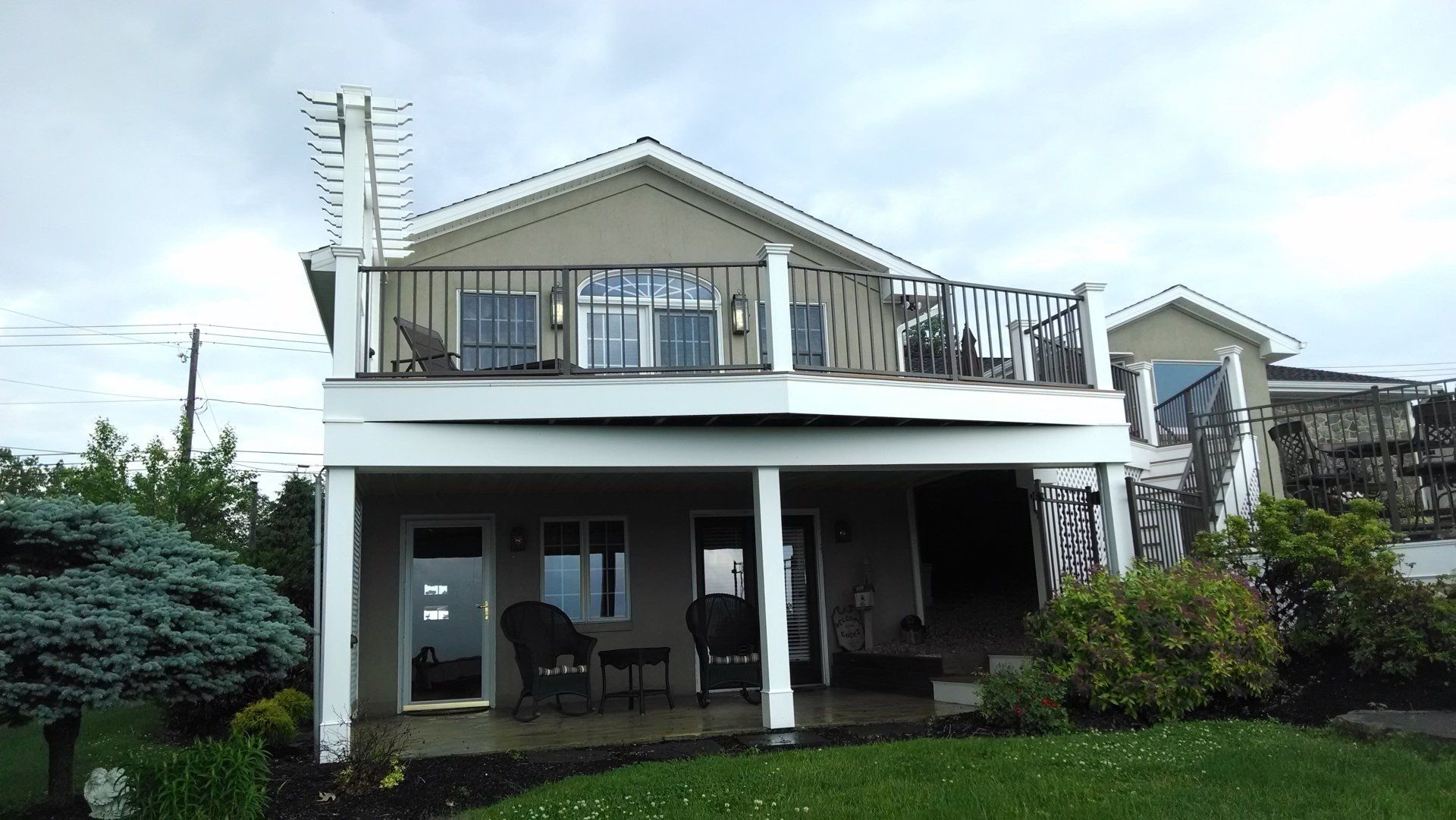 Two-story house with balcony, tan siding, black railing, on a cloudy day.