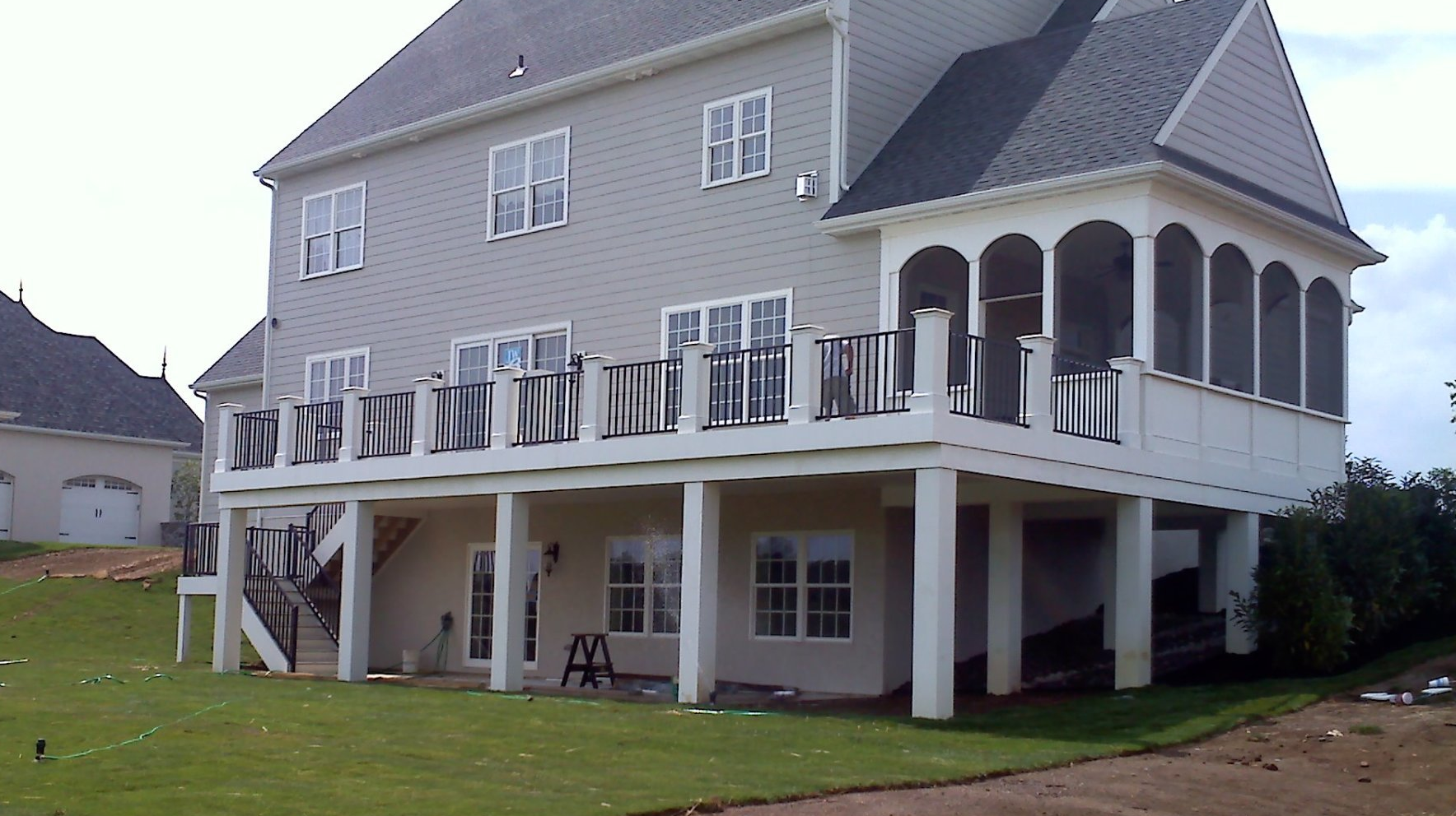 Two-story house with a large deck and screened porch overlooking a grassy yard.