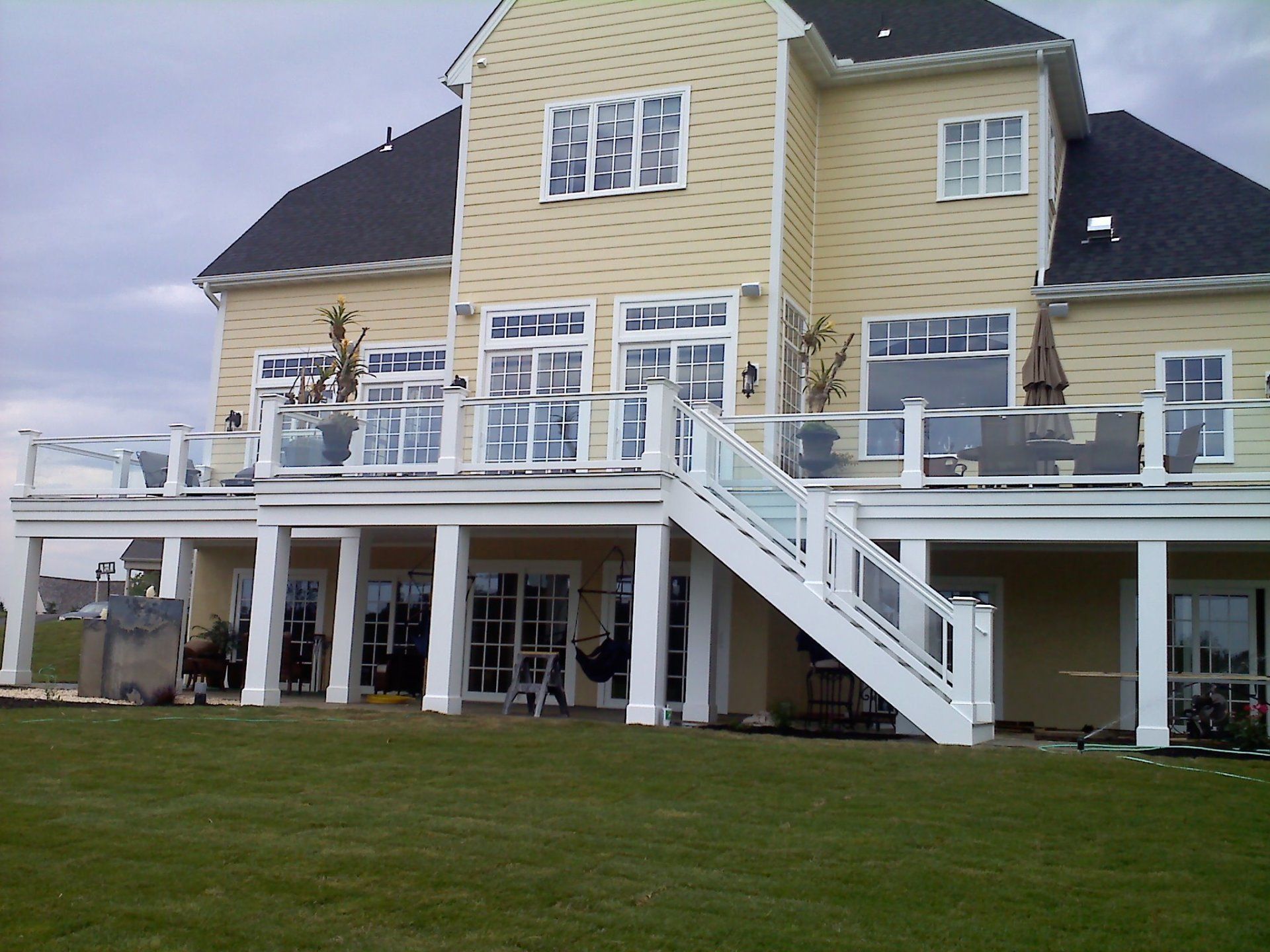 Yellow house with white deck and glass railings. Green lawn in front.