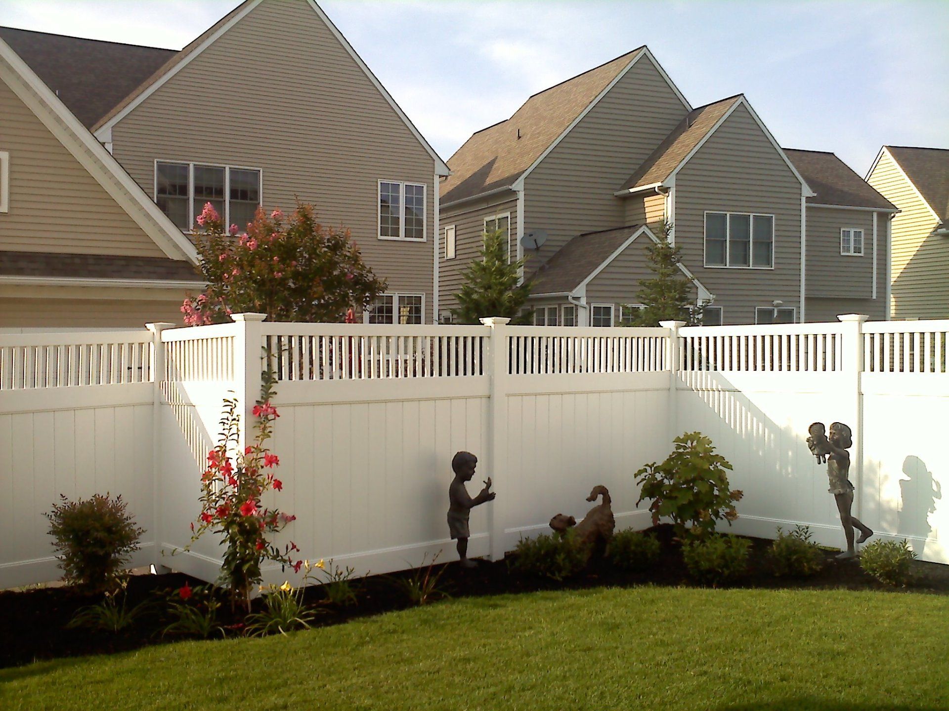 White fence with garden, statues, and houses in the background. Green lawn, blue sky in Lititz, PA.