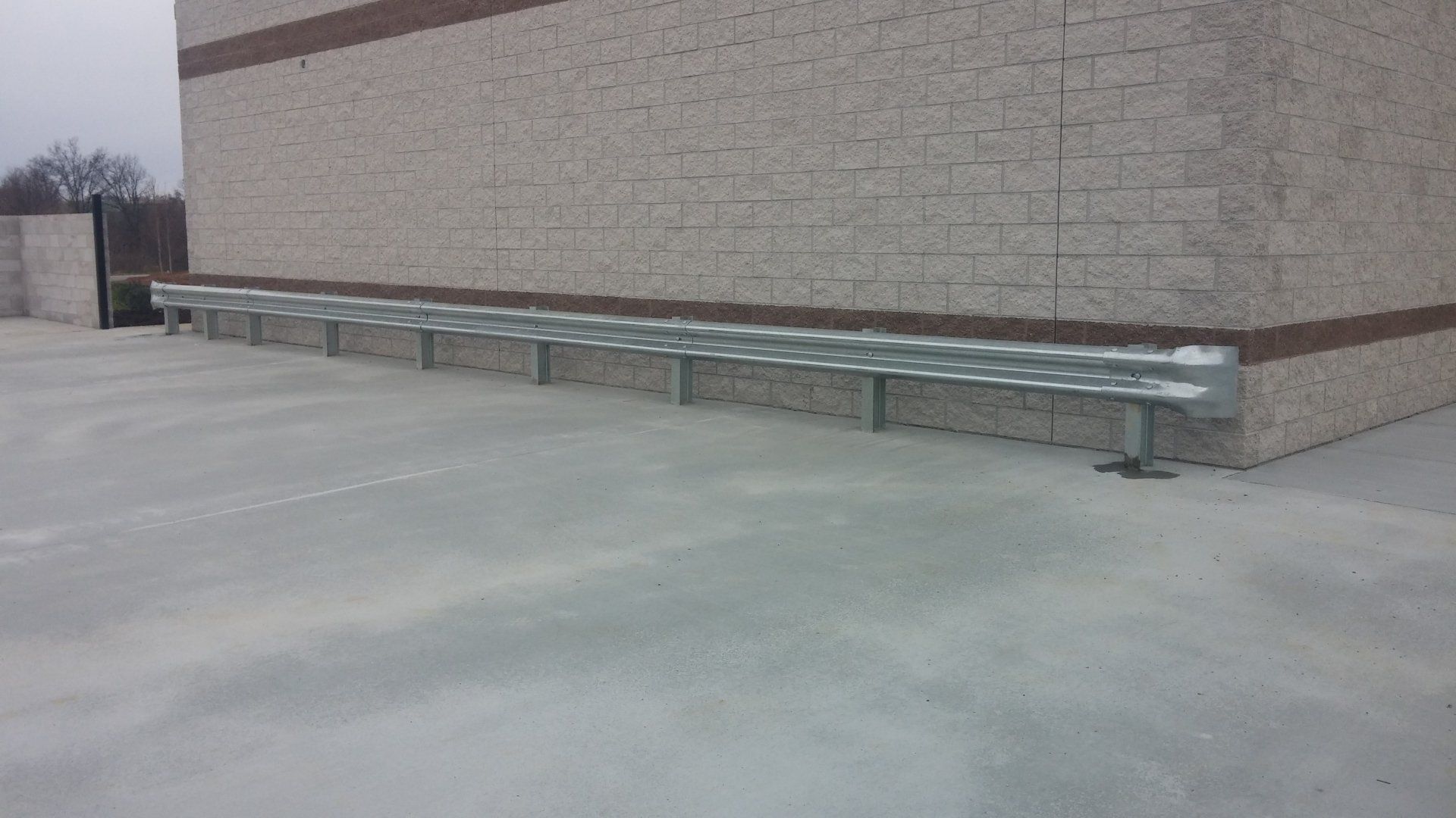 Metal barrier along a concrete floor in front of a brick wall.
