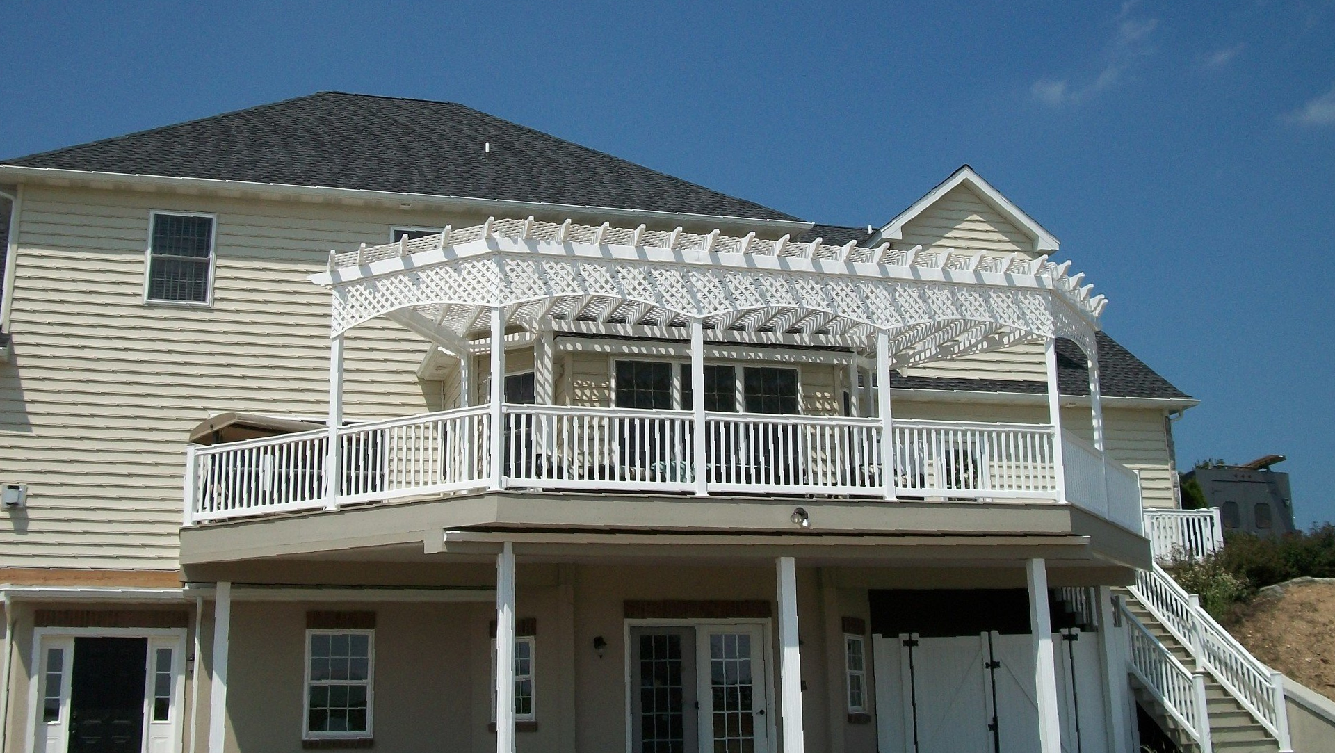 Two-story house with a white deck and pergola; blue sky background.