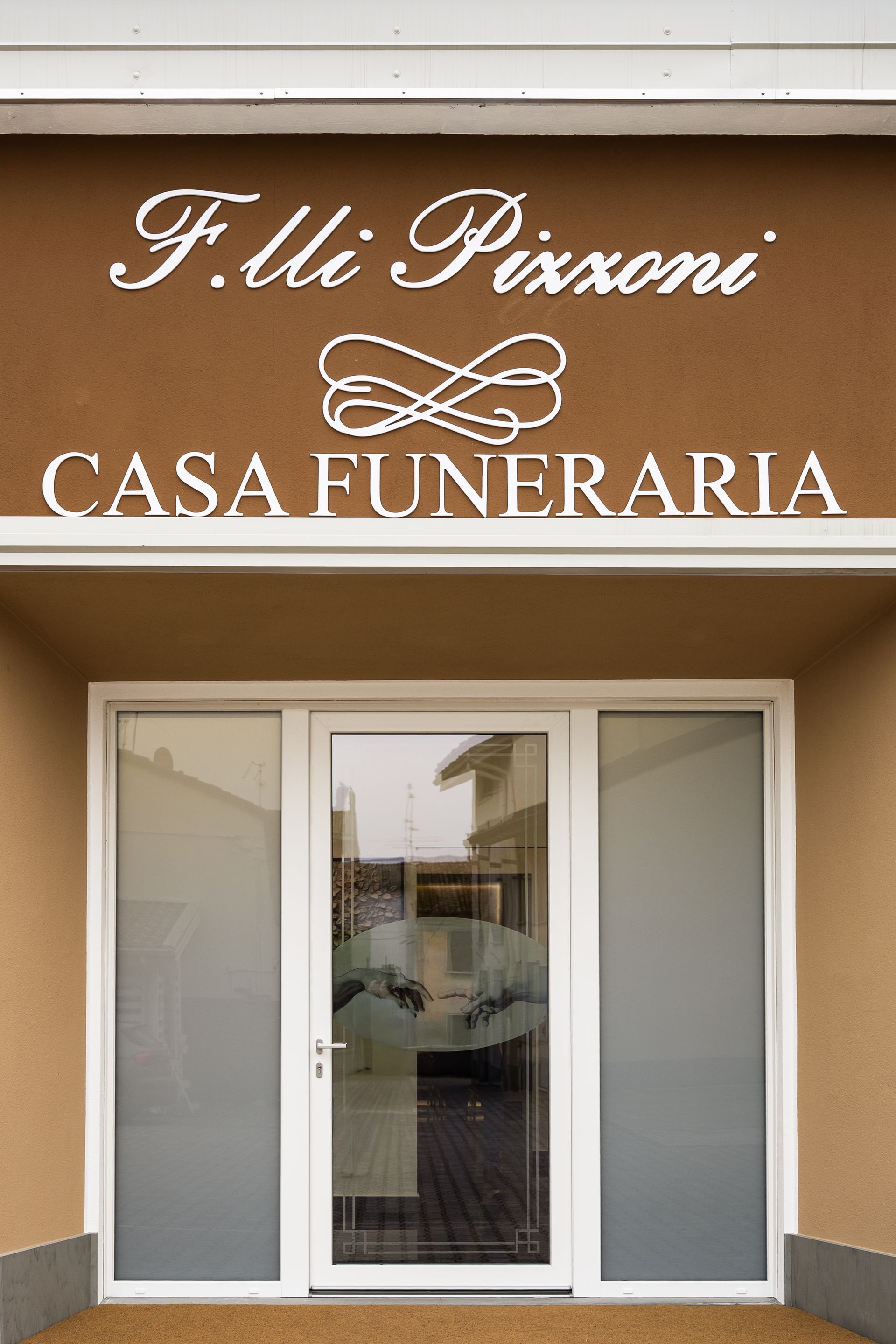 Insegna per l'impresa di pompe funebri F.lli Pizzoni: scritta bianca su stucco marrone sopra una porta a vetri.