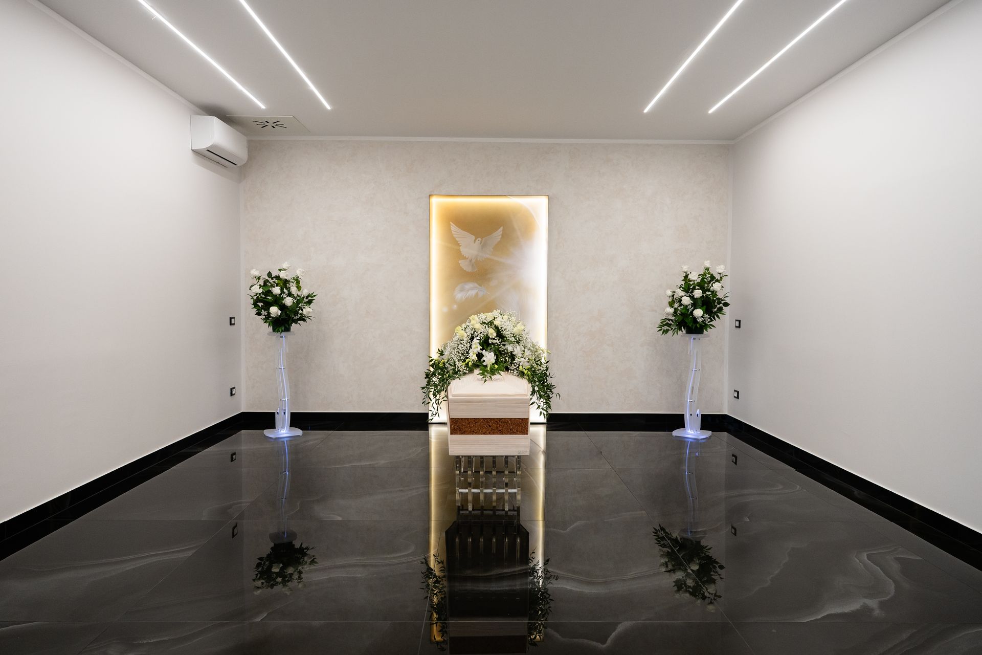 L'interno di un'agenzia funebre moderna presenta una bara, fiori e uno sfondo decorativo con una colomba.