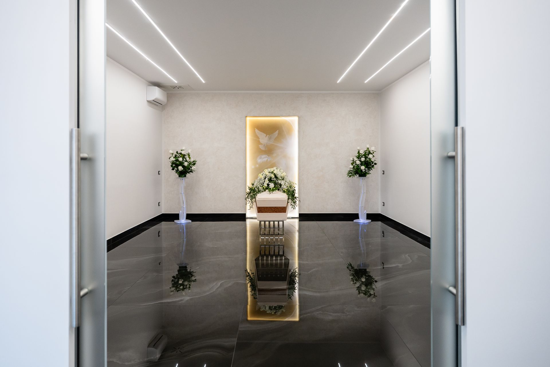 Una cappella moderna: al centro c'è la bara, circondata da composizioni floreali e da un'architettura elegante.