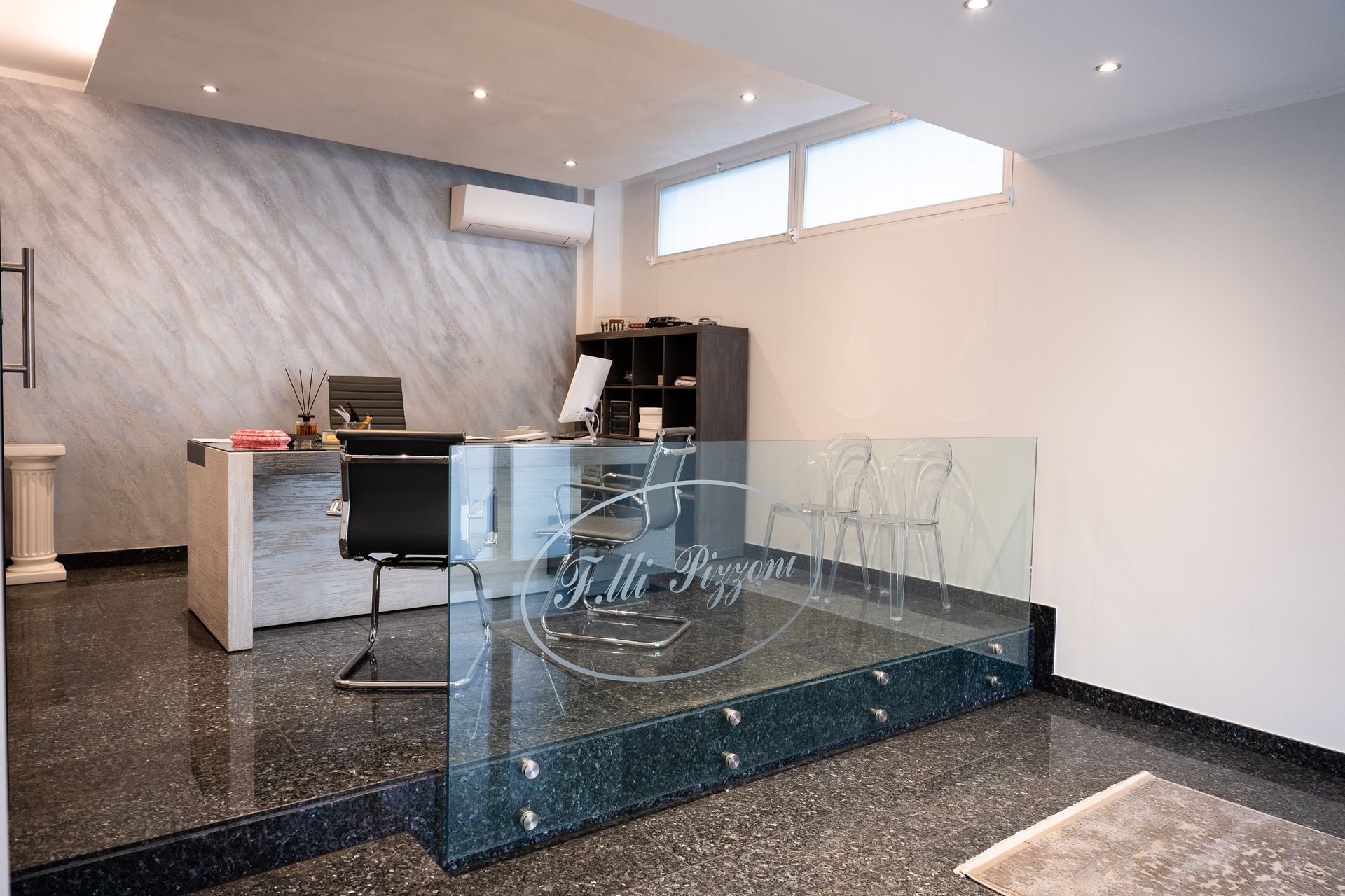 Area reception con scrivania in vetro, parete in marmo grigio, pavimento nero e materiale per ufficio.