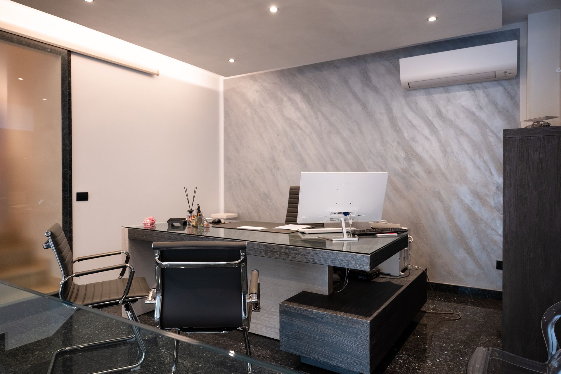 Ufficio con scrivania, sedia, computer e parete in marmo. Unità di aria condizionata a parete.