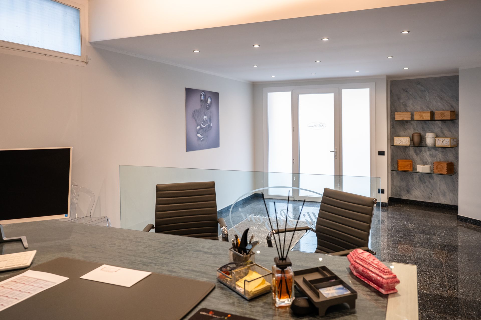 Ufficio moderno con tavolo in vetro, sedie nere, opere d'arte e accesso all'esterno.