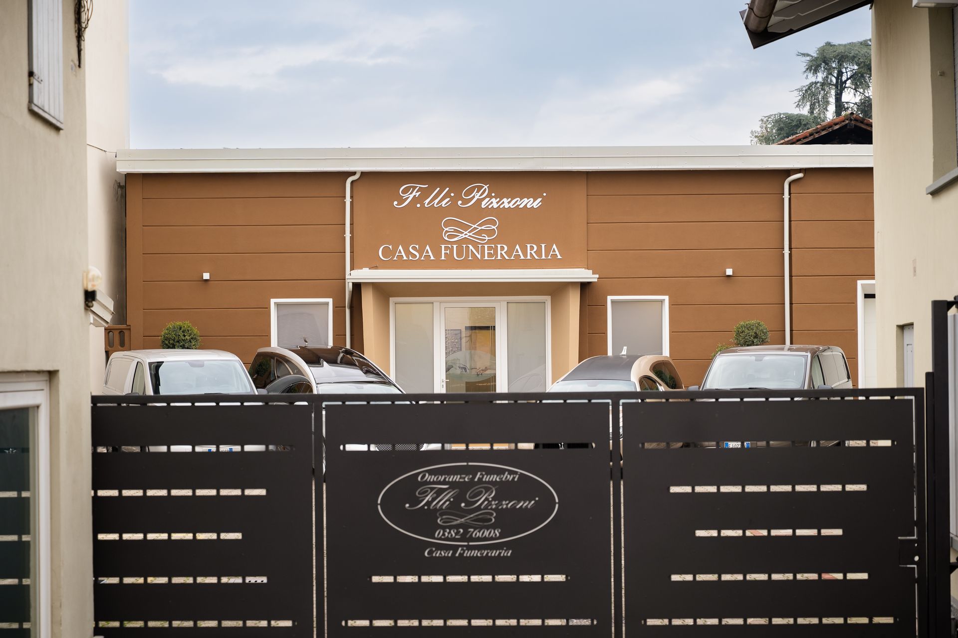 L'edificio marrone della Casa Funeraria è dietro un cancello nero; auto parcheggiate di fronte.