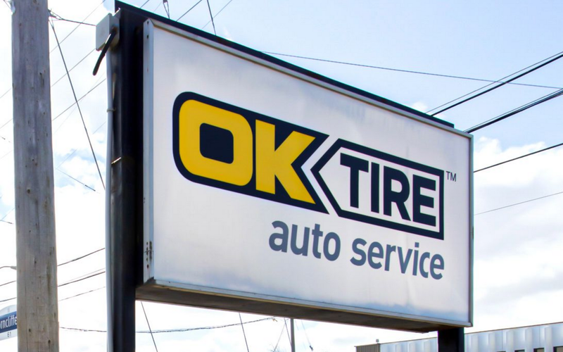 Sign for OK Tire auto service, with yellow and black logo on a white background.
