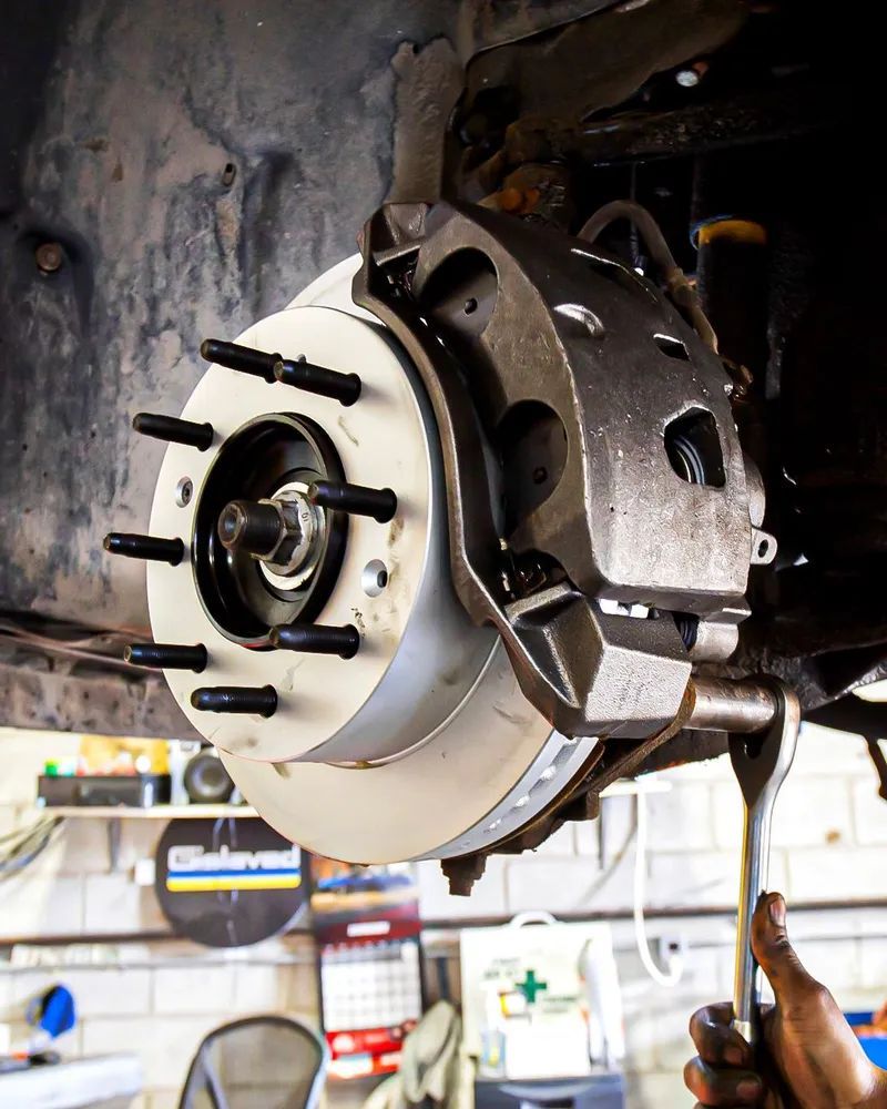 Car brake disc and caliper being worked on with a wrench in a garage.