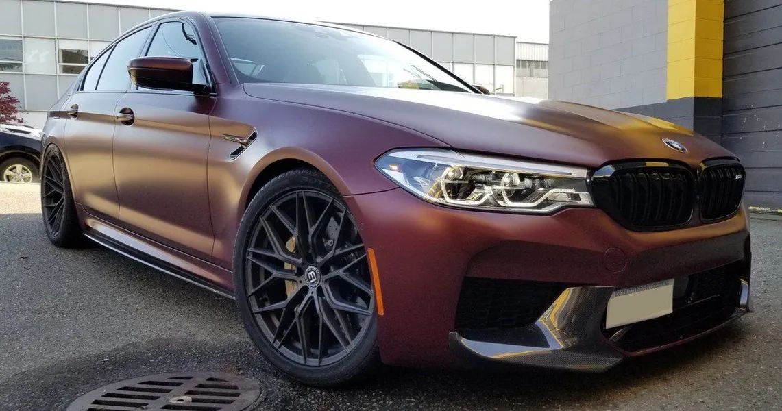 Maroon BMW M5 sports car, black wheels, parked in front of a building.