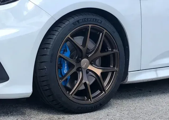 White car wheel with bronze rim, blue brake caliper, black tire, against white body.