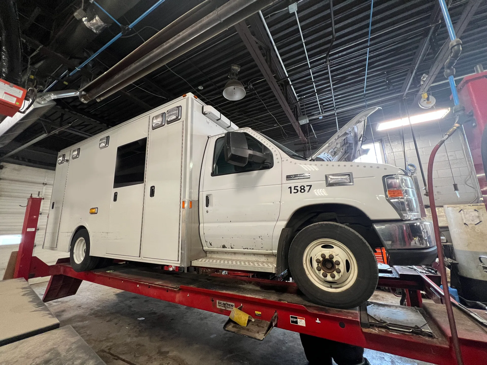 White ambulance on a red lift in a garage with the hood open.