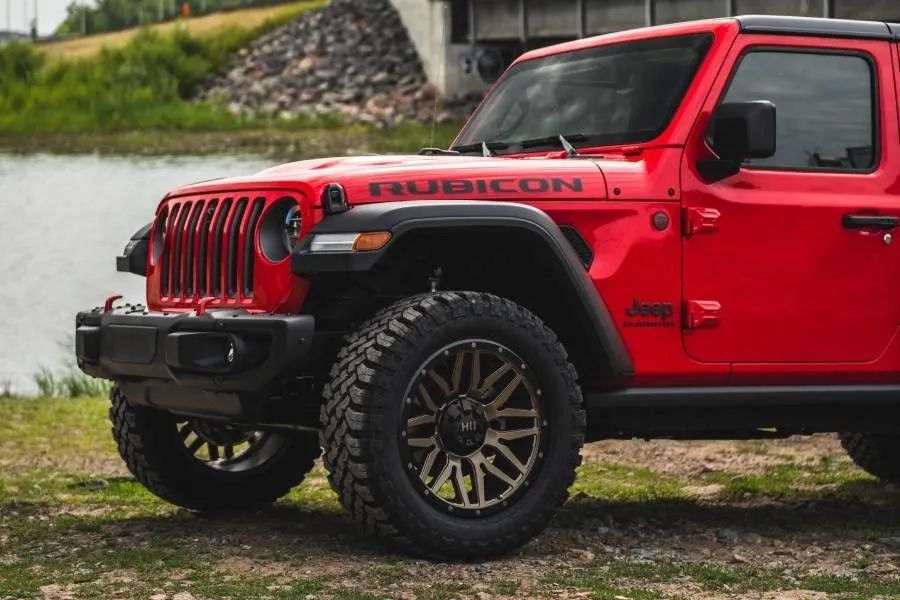 Red Jeep Rubicon off-road vehicle with large black tires parked near a body of water.