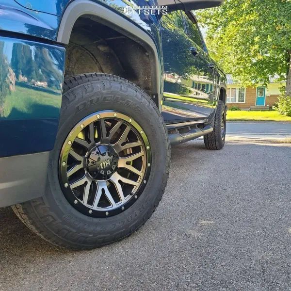 Blue truck with black and silver rims on a paved road. The truck is parked near a house with a blue door.