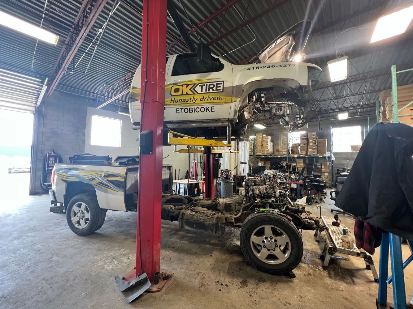 A truck in a repair shop is being worked on. The cab is raised, and the frame is exposed.