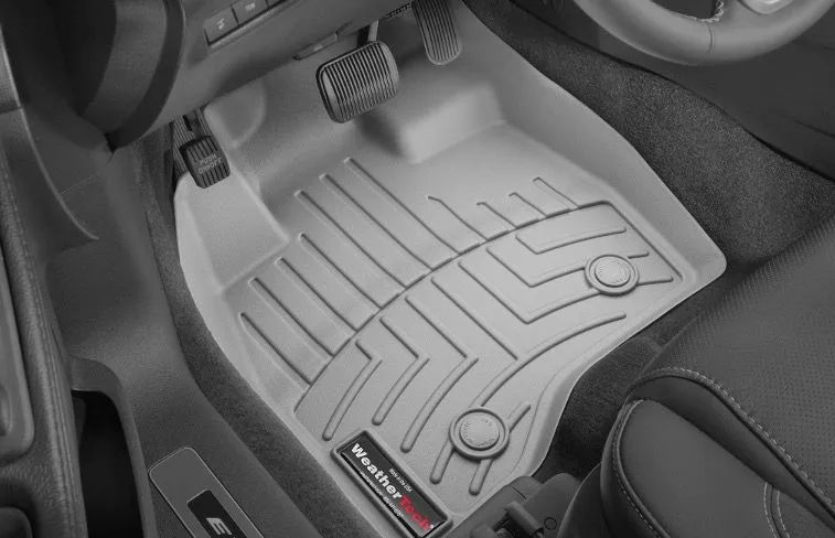 Beige car floor mat in a vehicle interior, covering the driver's side floor, near the pedals.