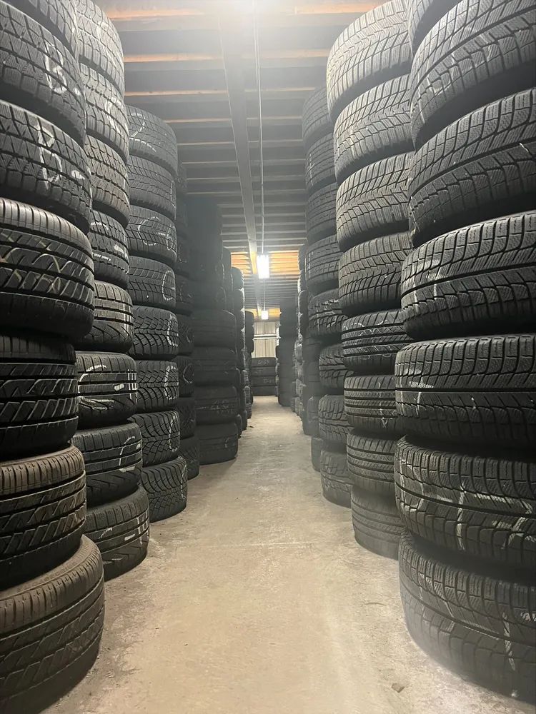 Tires stacked high in a warehouse, forming aisles. The setting is dimly lit.
