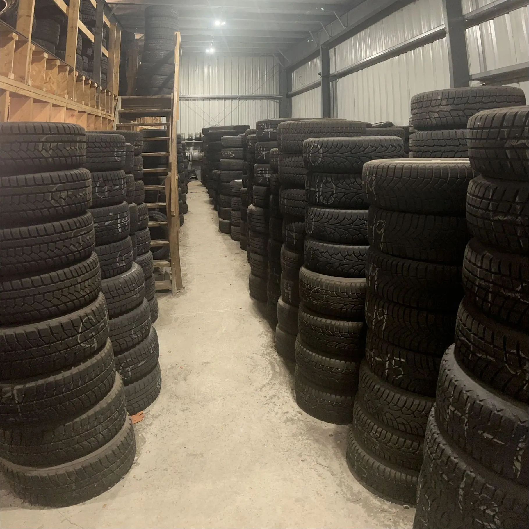 Stacks of tires stored inside a warehouse. Dark tires are packed tightly in rows.
