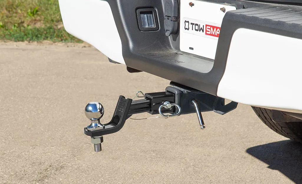Close-up of a white truck's rear bumper with a black trailer hitch, ball, and safety chains.