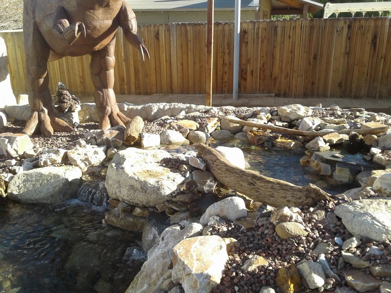 A statue of a dinosaur is standing in front of a wooden fence