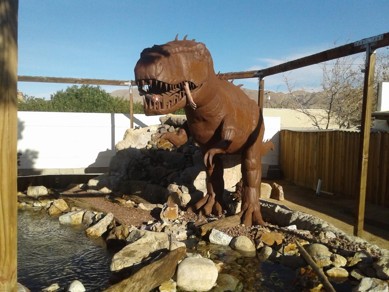 A statue of a dinosaur standing next to a pond