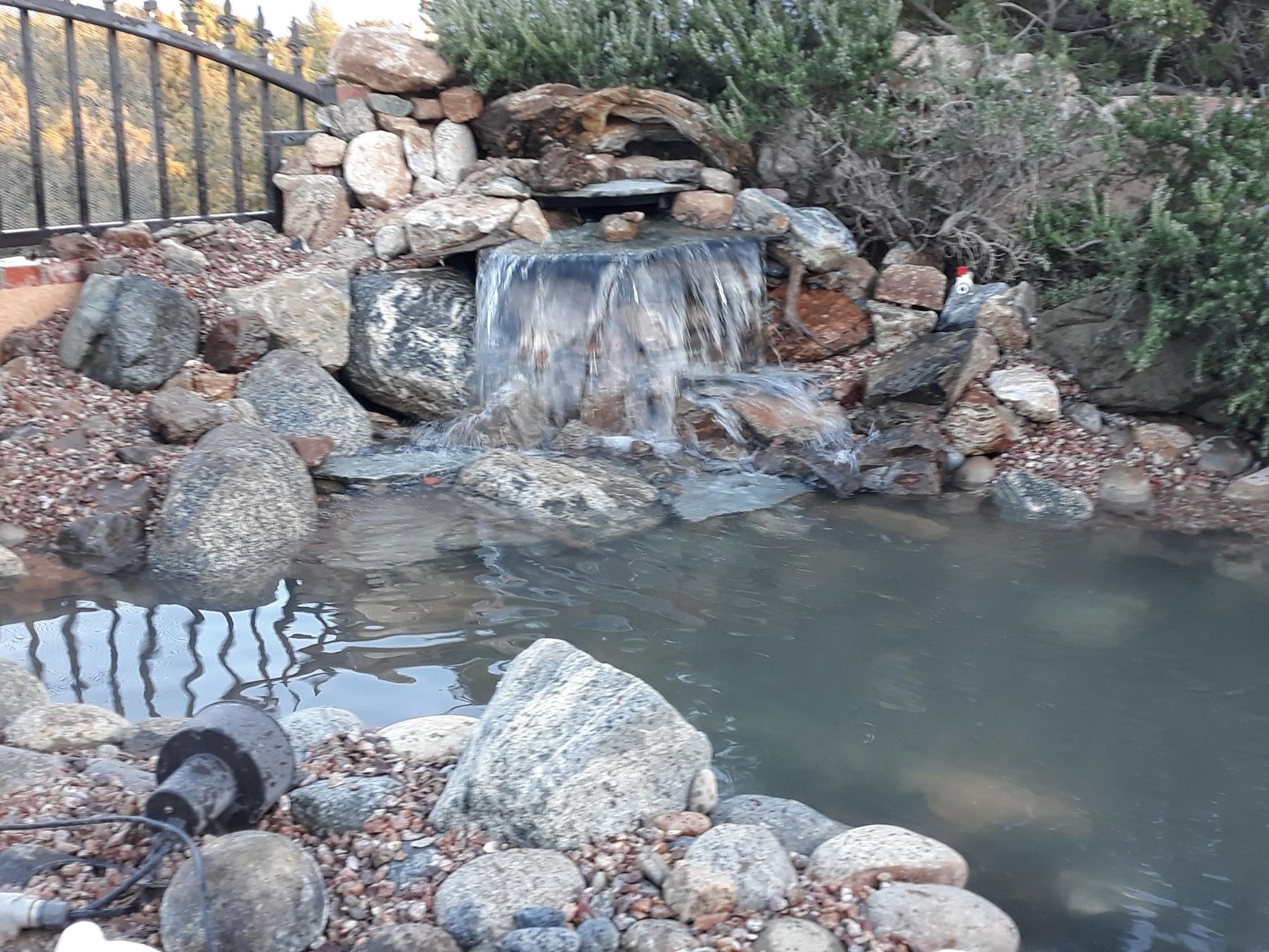 There is a waterfall in the middle of a pond surrounded by rocks.