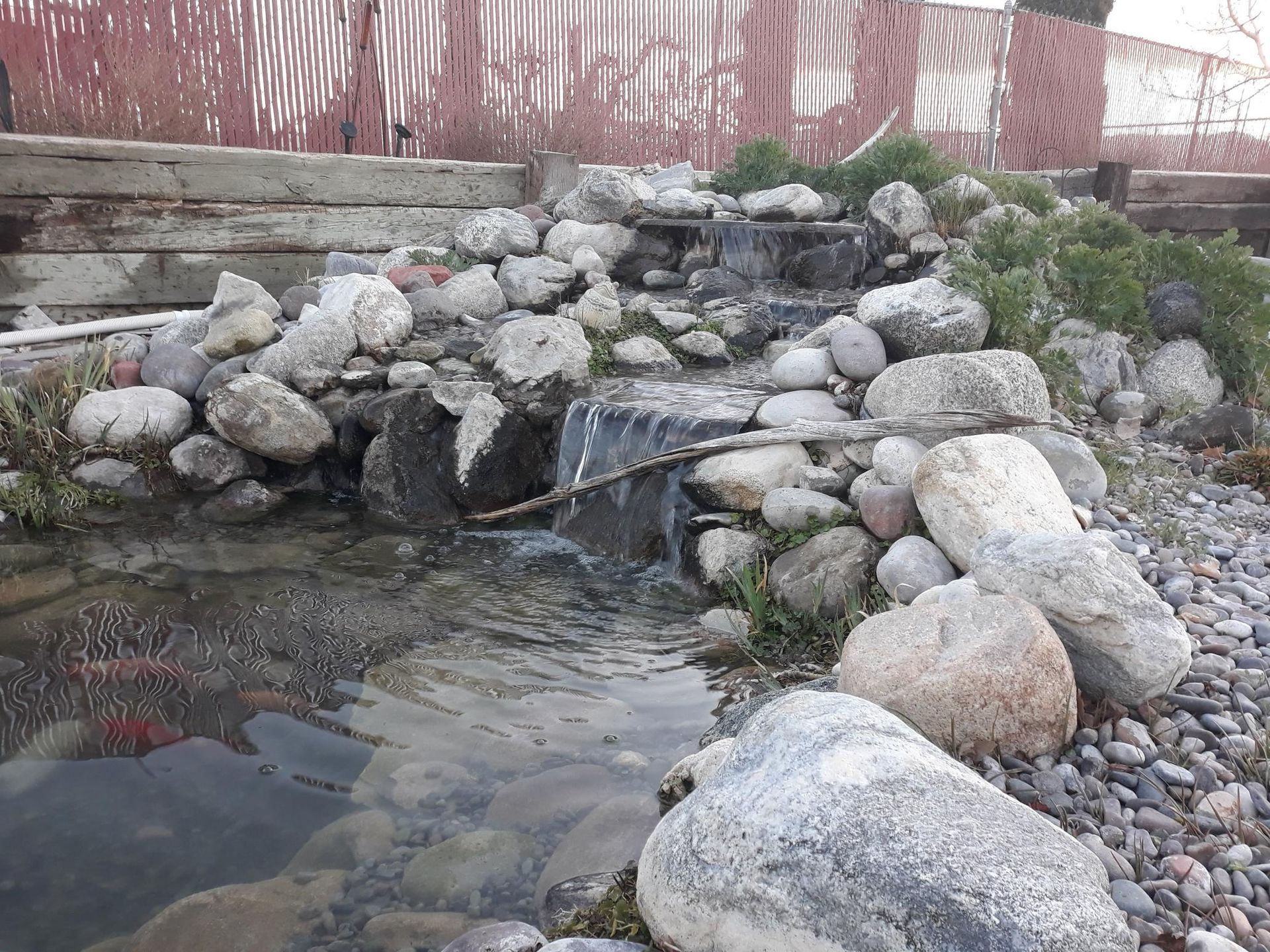 A small waterfall is surrounded by rocks and a fence.