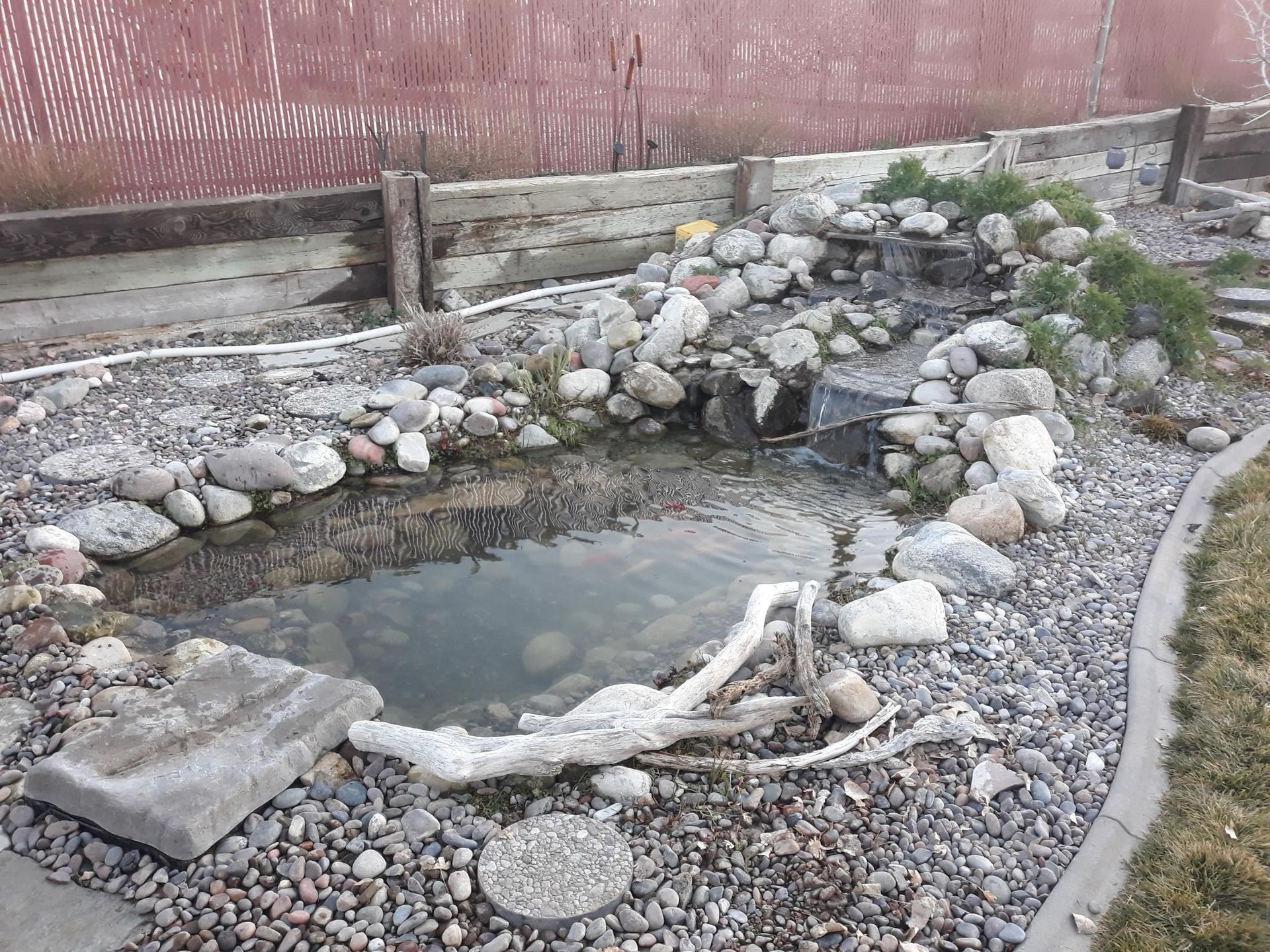 A small pond surrounded by rocks and a fence