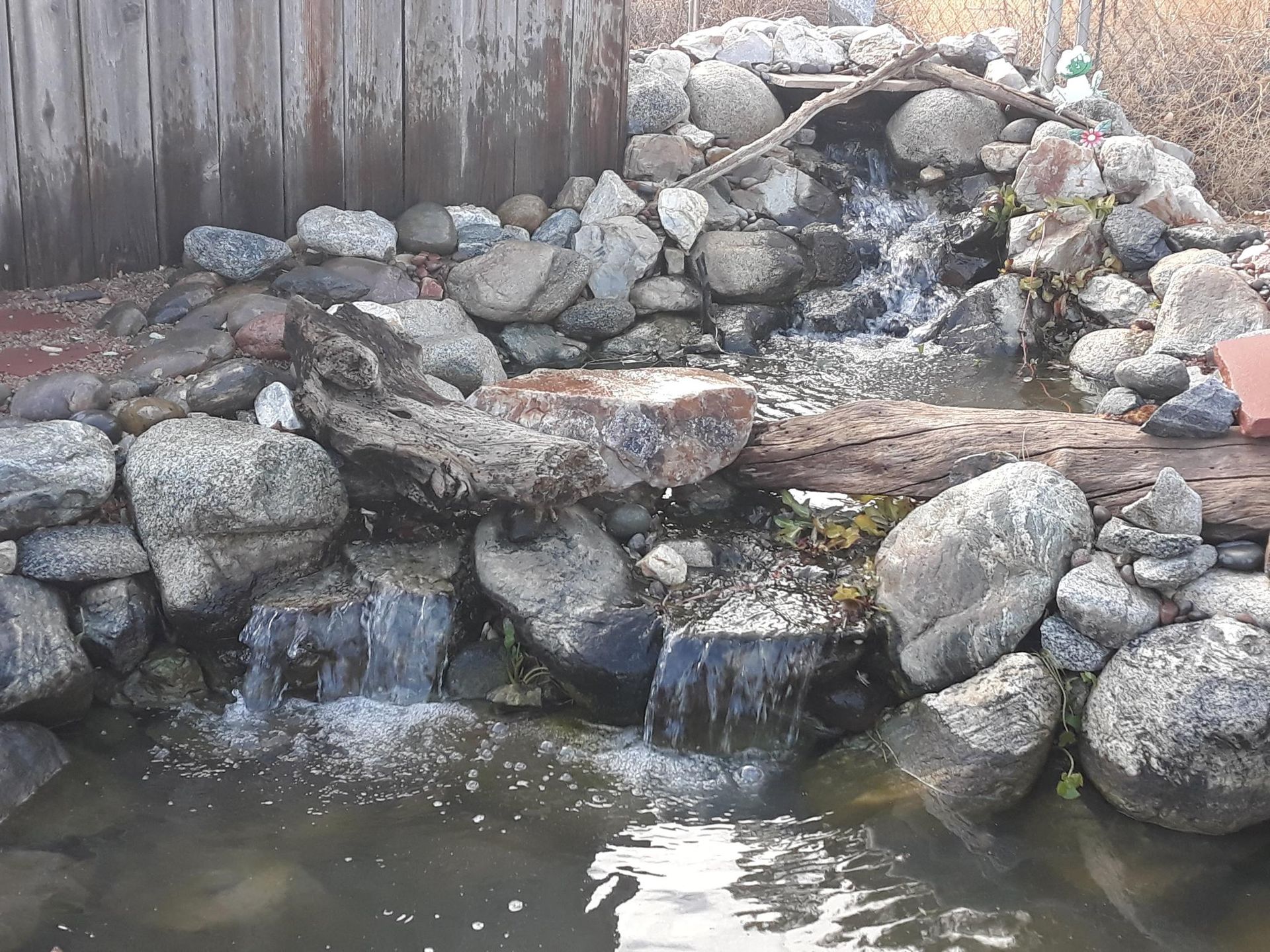 A waterfall is surrounded by rocks and a wooden fence