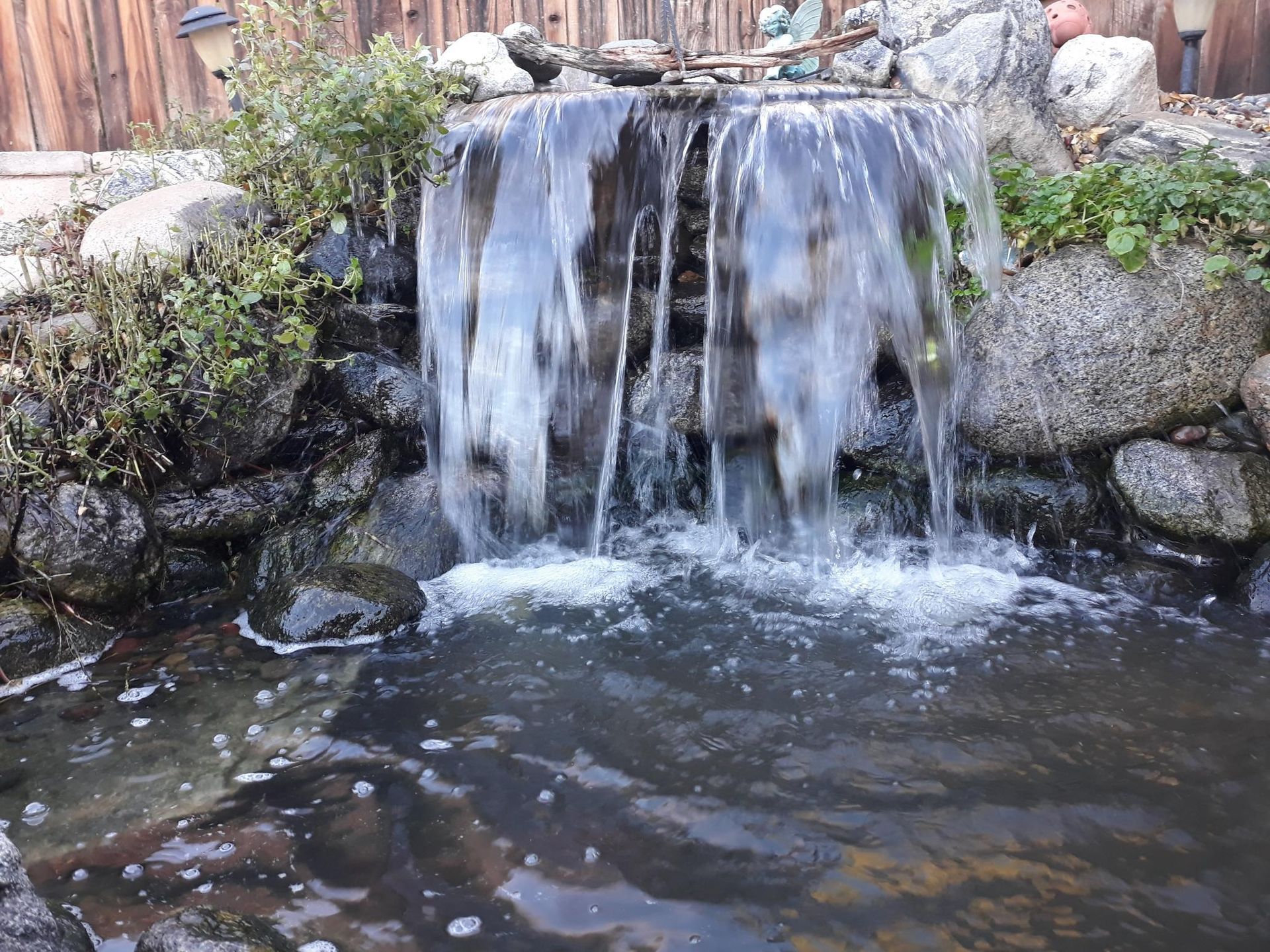 A small waterfall is surrounded by rocks and plants in a pond.