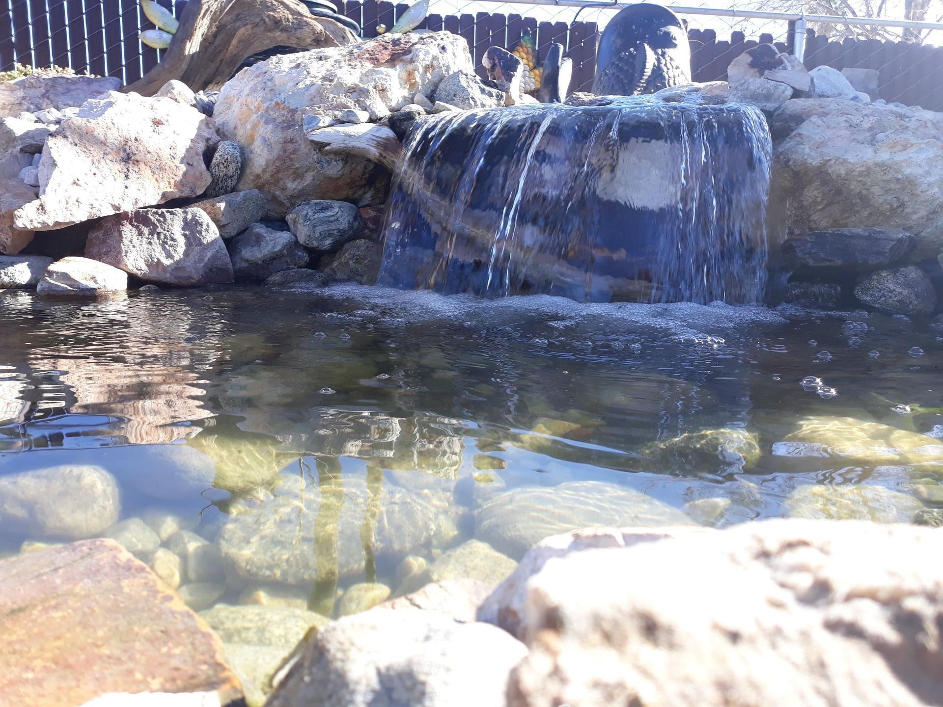 A small waterfall is surrounded by rocks in a pond