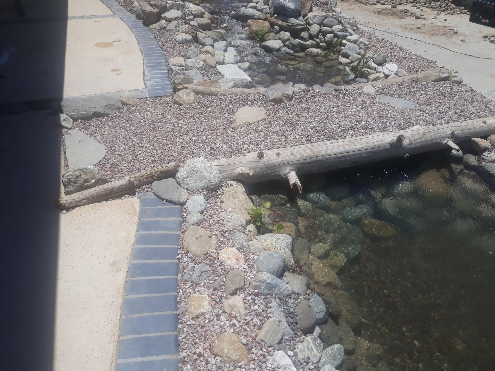 A pond surrounded by rocks and gravel next to a sidewalk