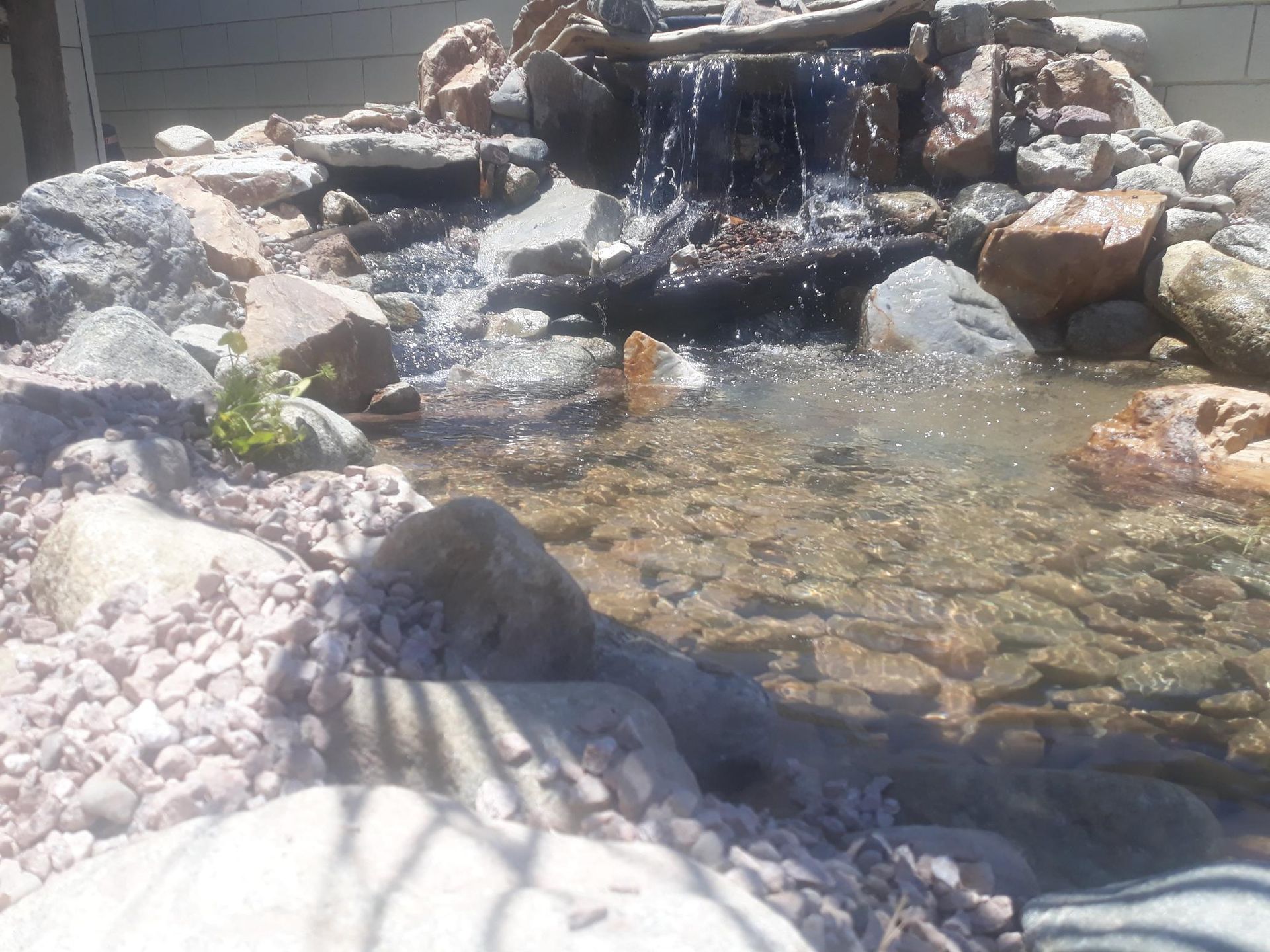 A waterfall is surrounded by rocks and water in a pond.