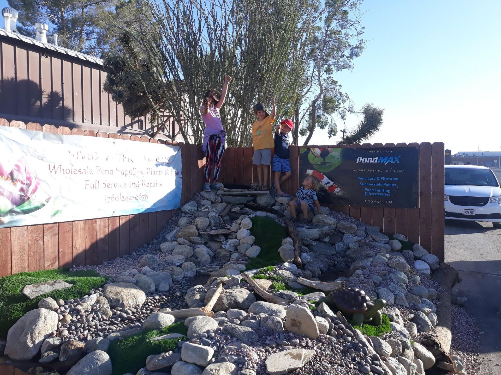 A group of children are playing on a rocky hill near a fence.
