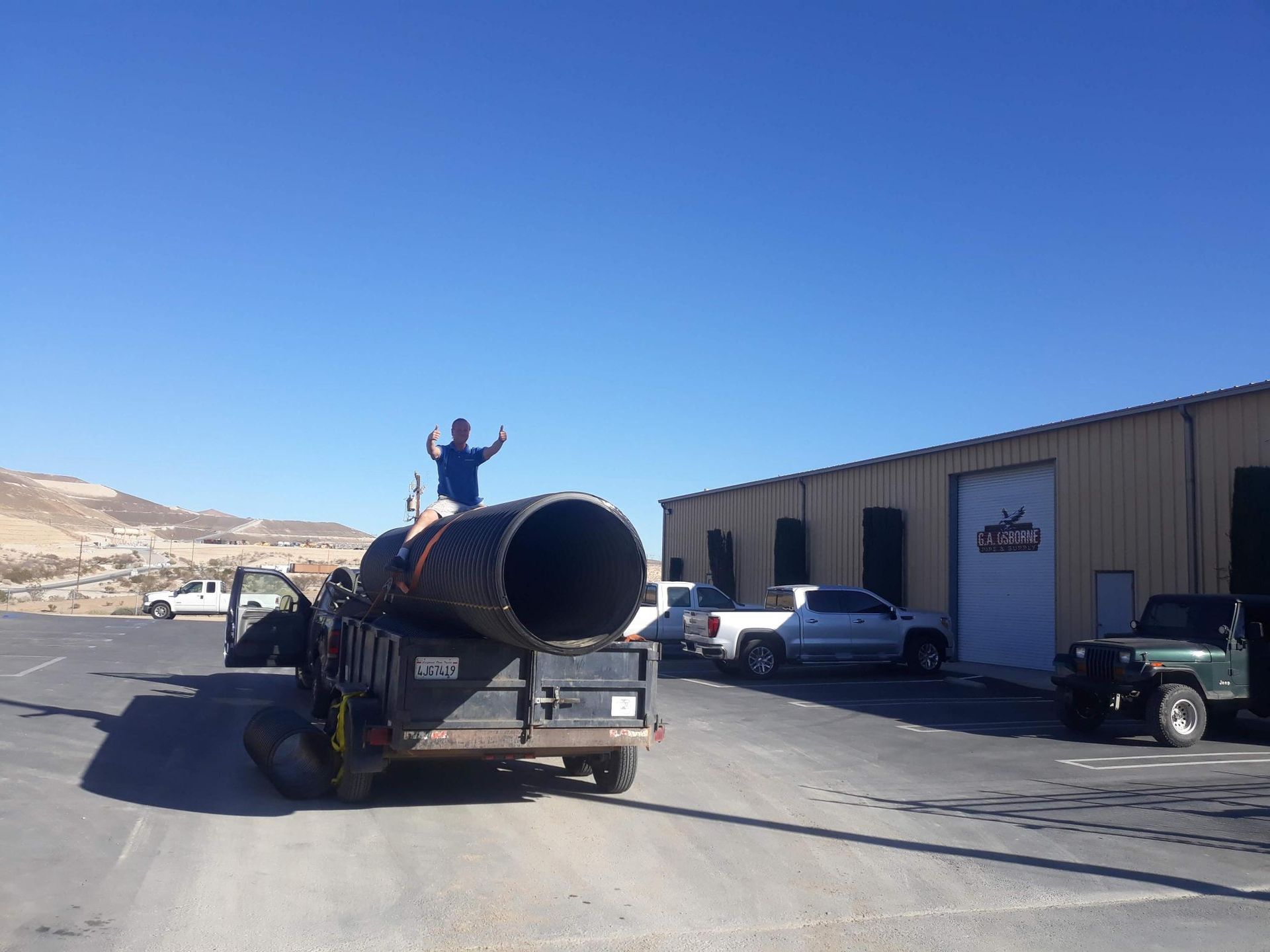 A man is standing on top of a truck carrying a large pipe