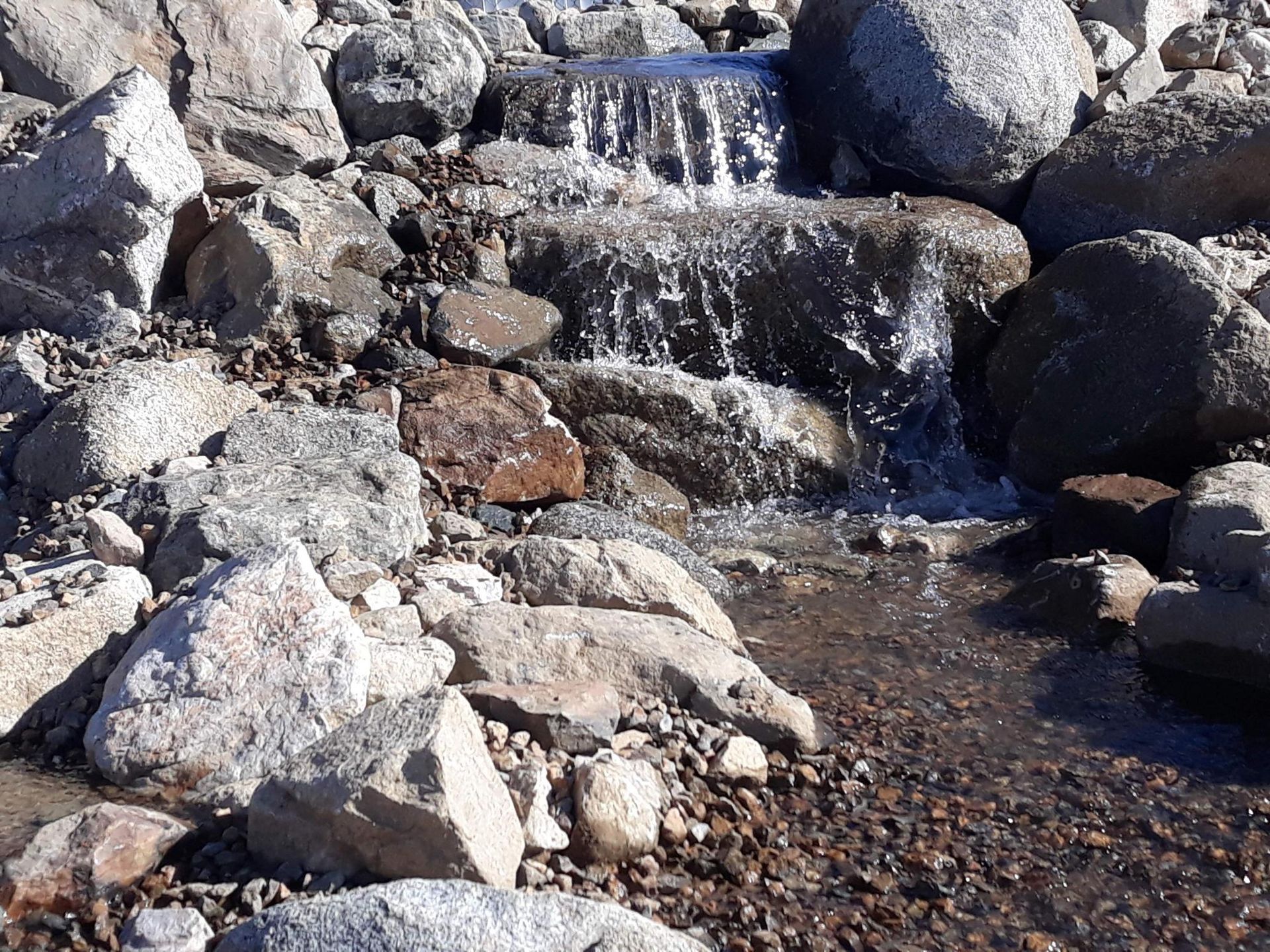 A small waterfall is surrounded by rocks and gravel.