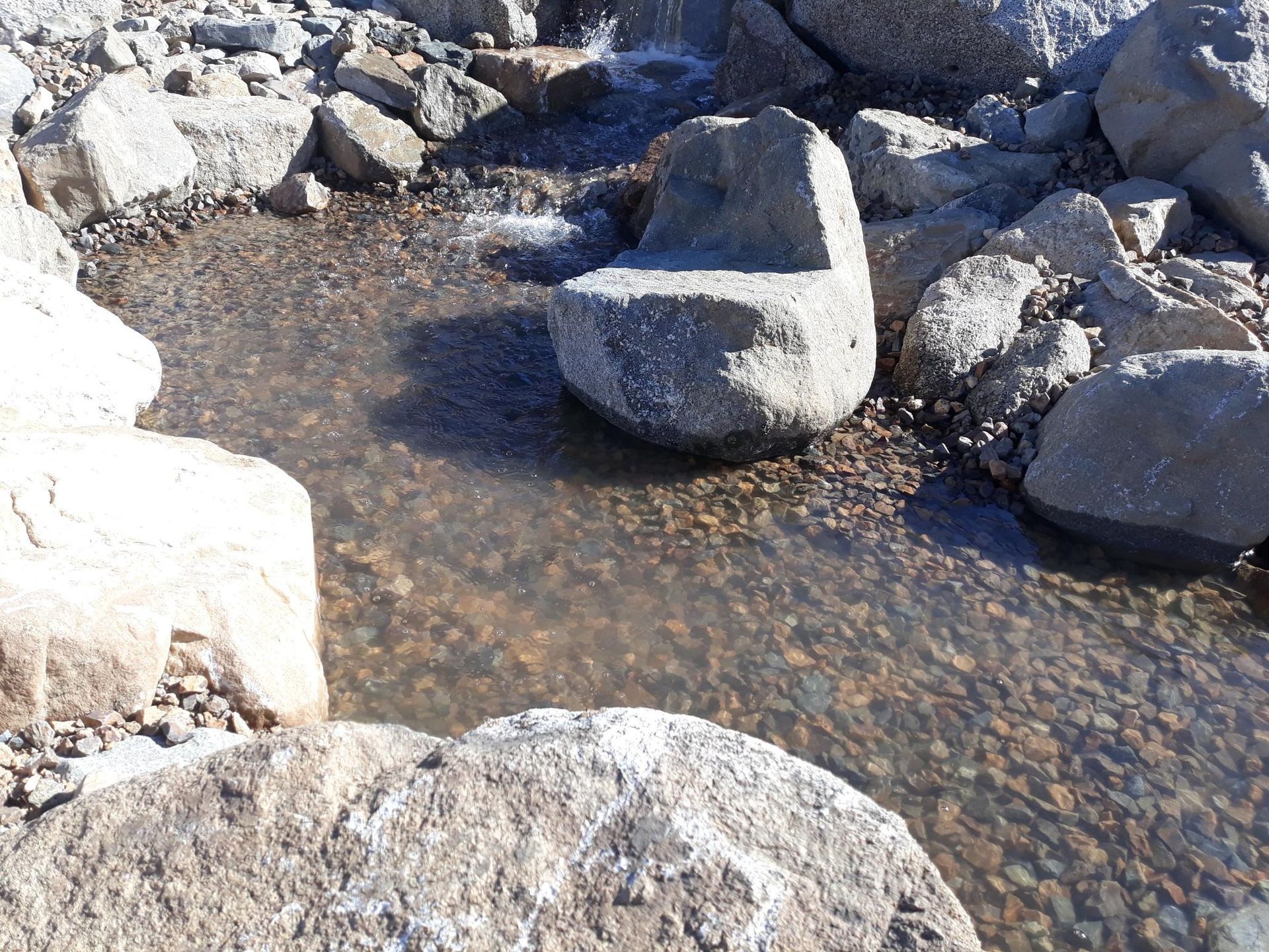 A rock in the middle of a river surrounded by rocks